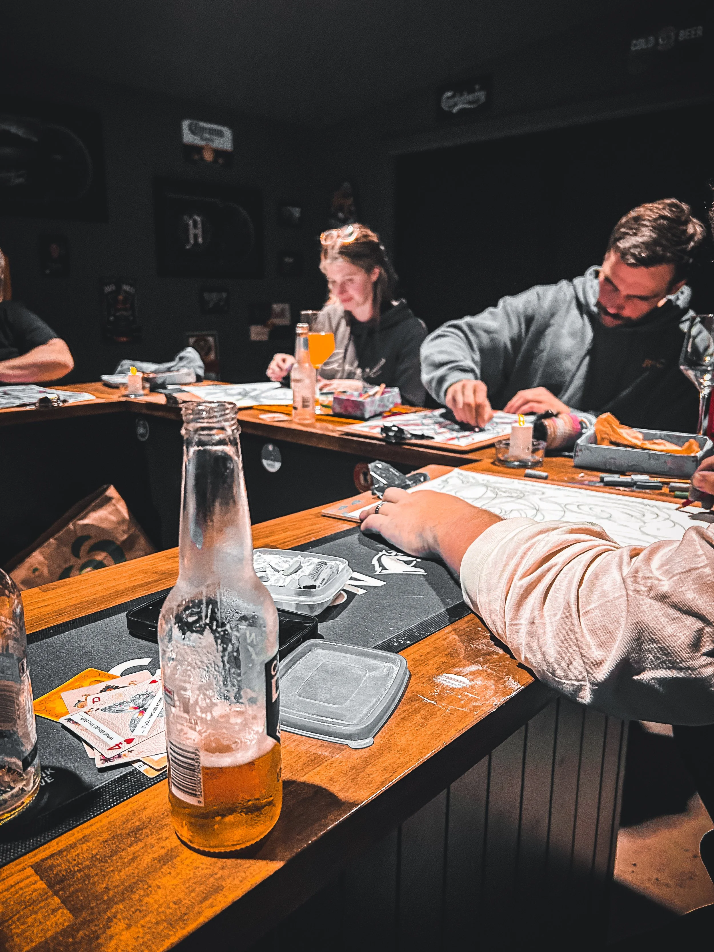 People sitting at a wooden table in a dimly lit restaurant, with drinks, cards, and game pieces on the table, engaged in a social activity.