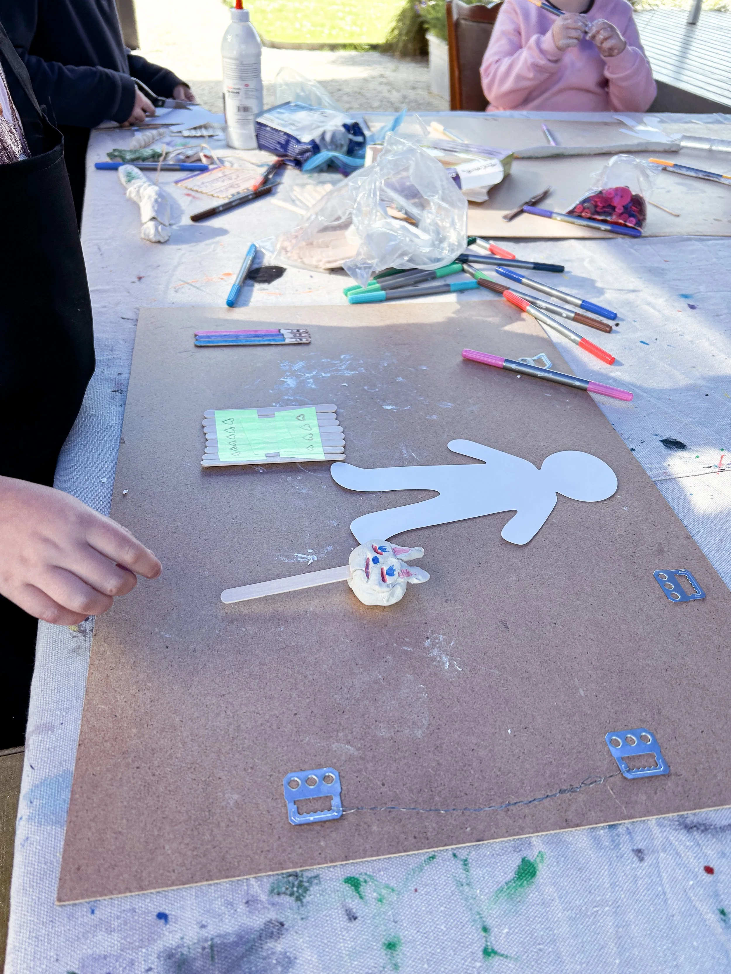 Children's arts and crafts project table with paper cutouts, markers, and craft supplies outdoors.