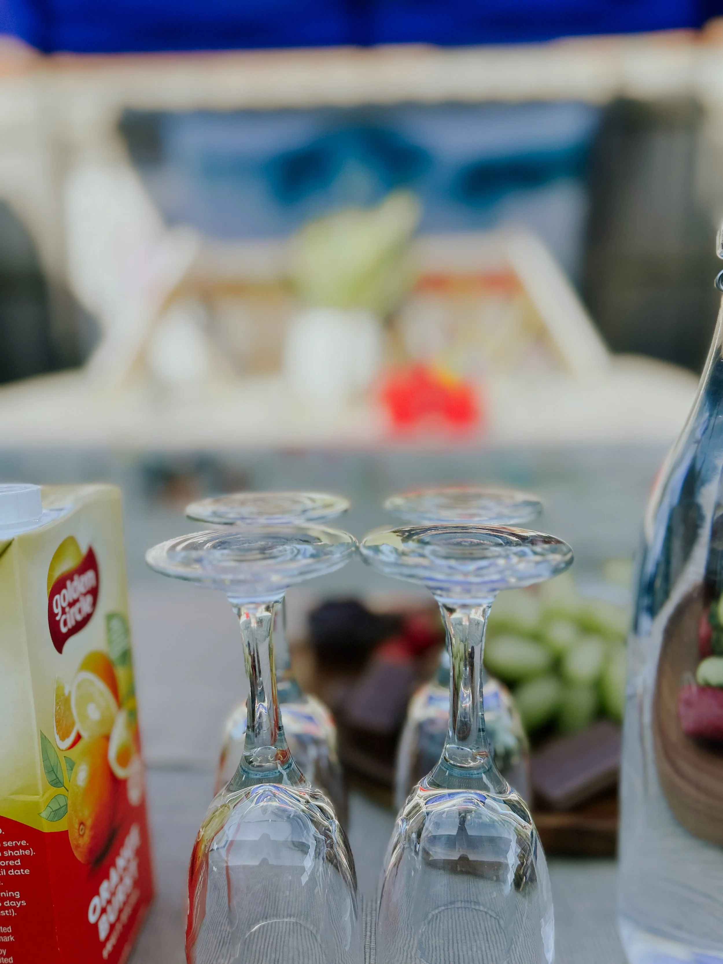 Empty wine glasses upside down on a table surrounded by snacks including chocolate and fruit, with juice boxes and a pitcher nearby.