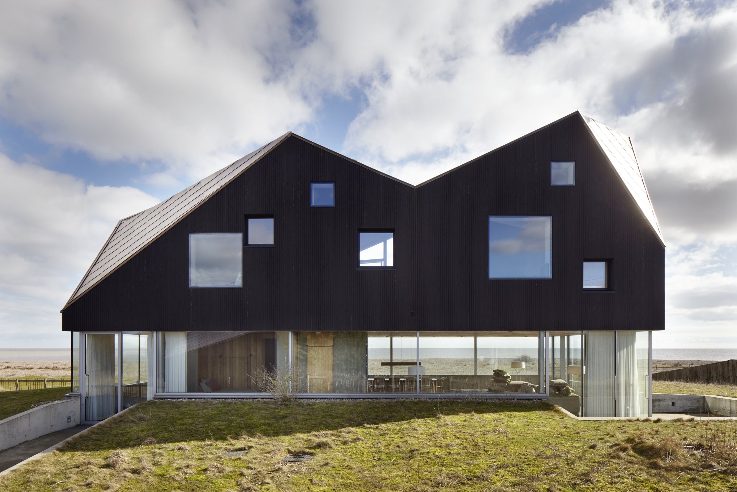 Exterior image of large modern contemporary house, with interior visible through windows and large angled black roof,  perfect for exterior filming and lifestyle shoots