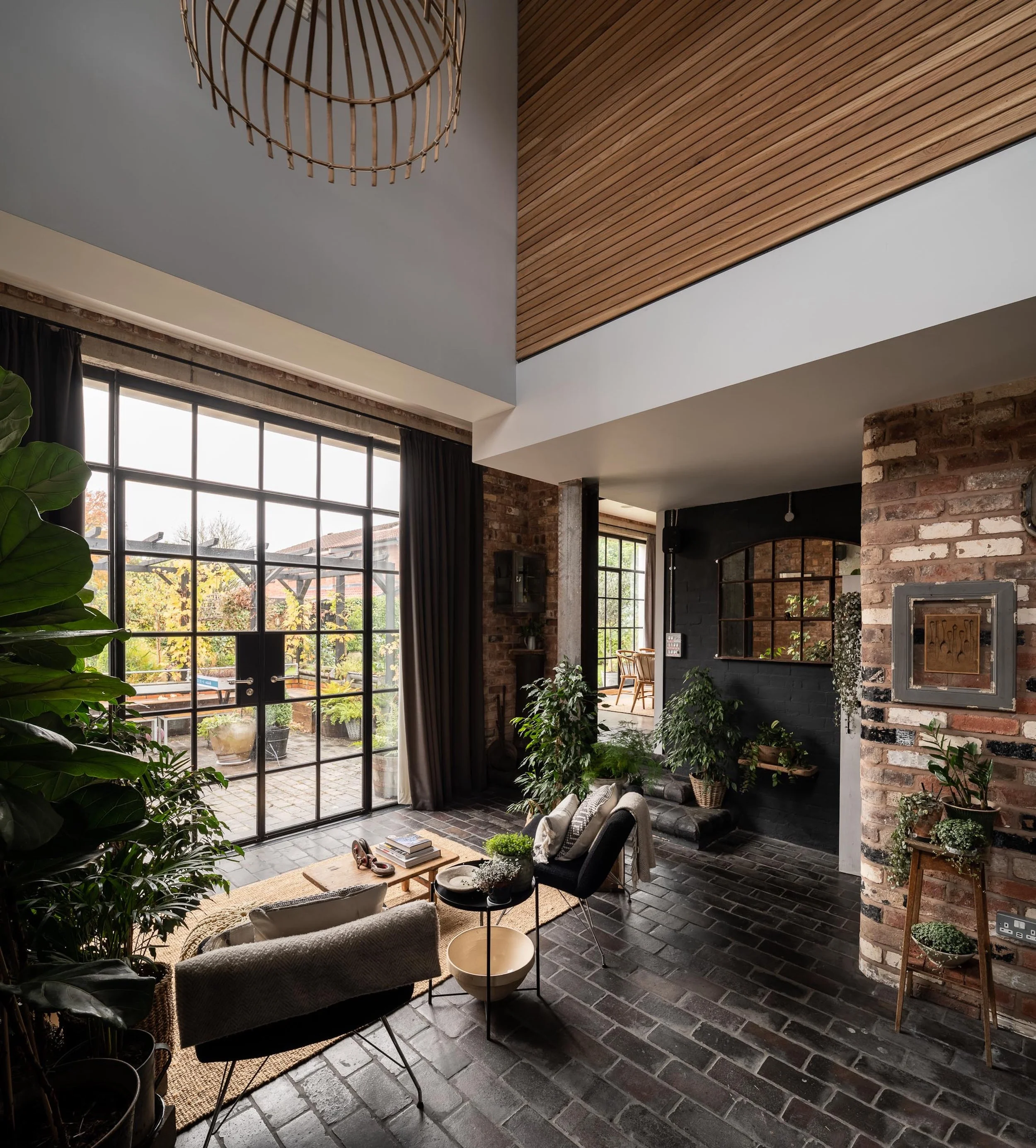 Living room with brick walls, large glass door leading to a patio, indoor plants, and modern furniture.