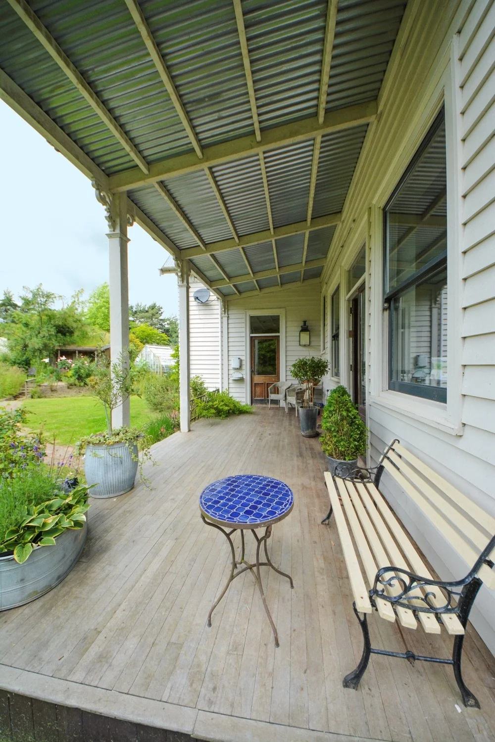 A porch with outdoor seating, potted plants, and a view of a garden in the background.