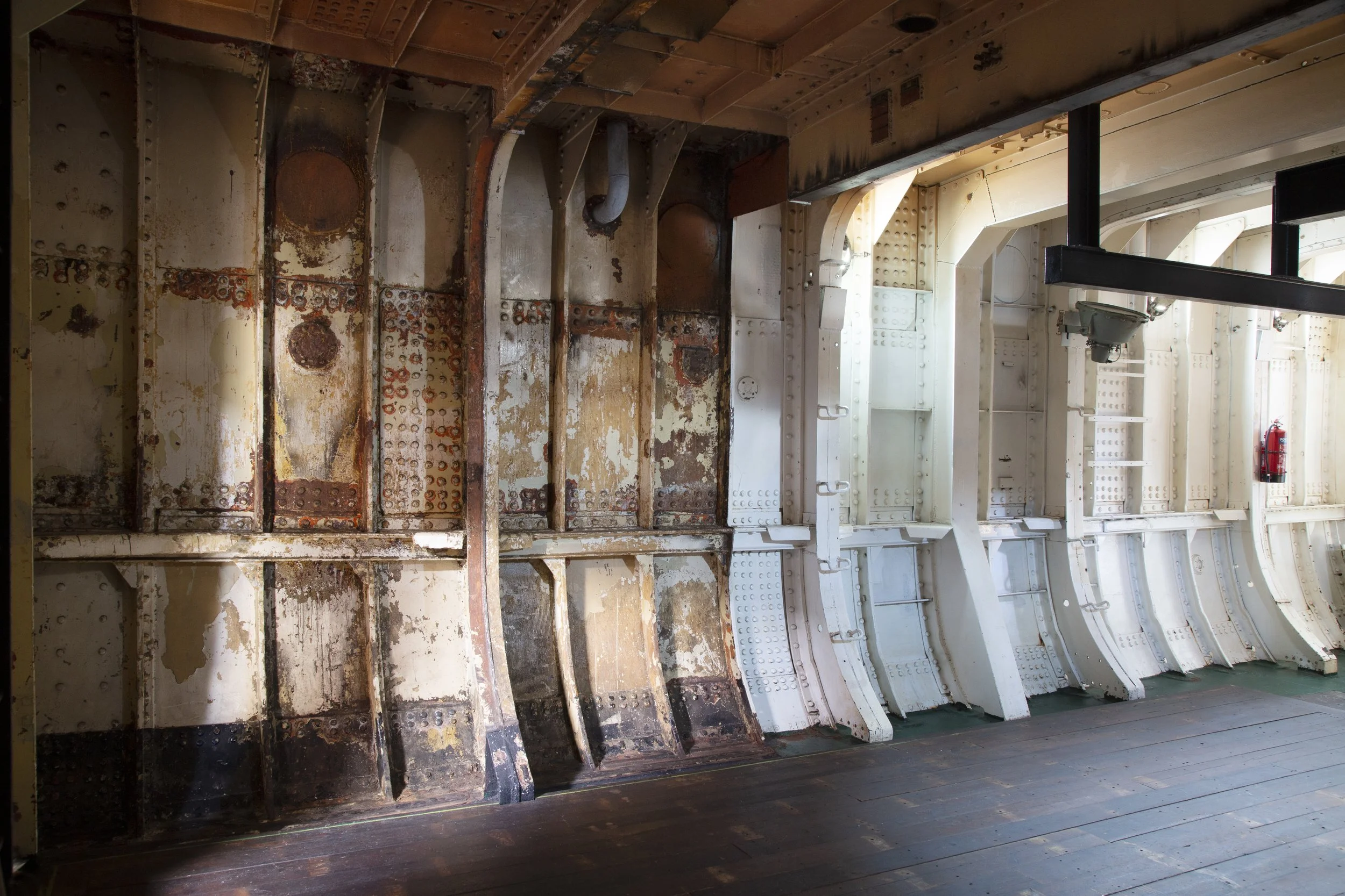 Interior of an aircraft fuselage showing the contrast between rusty, worn-left side and freshly painted right side, with visible rivets and structural elements.