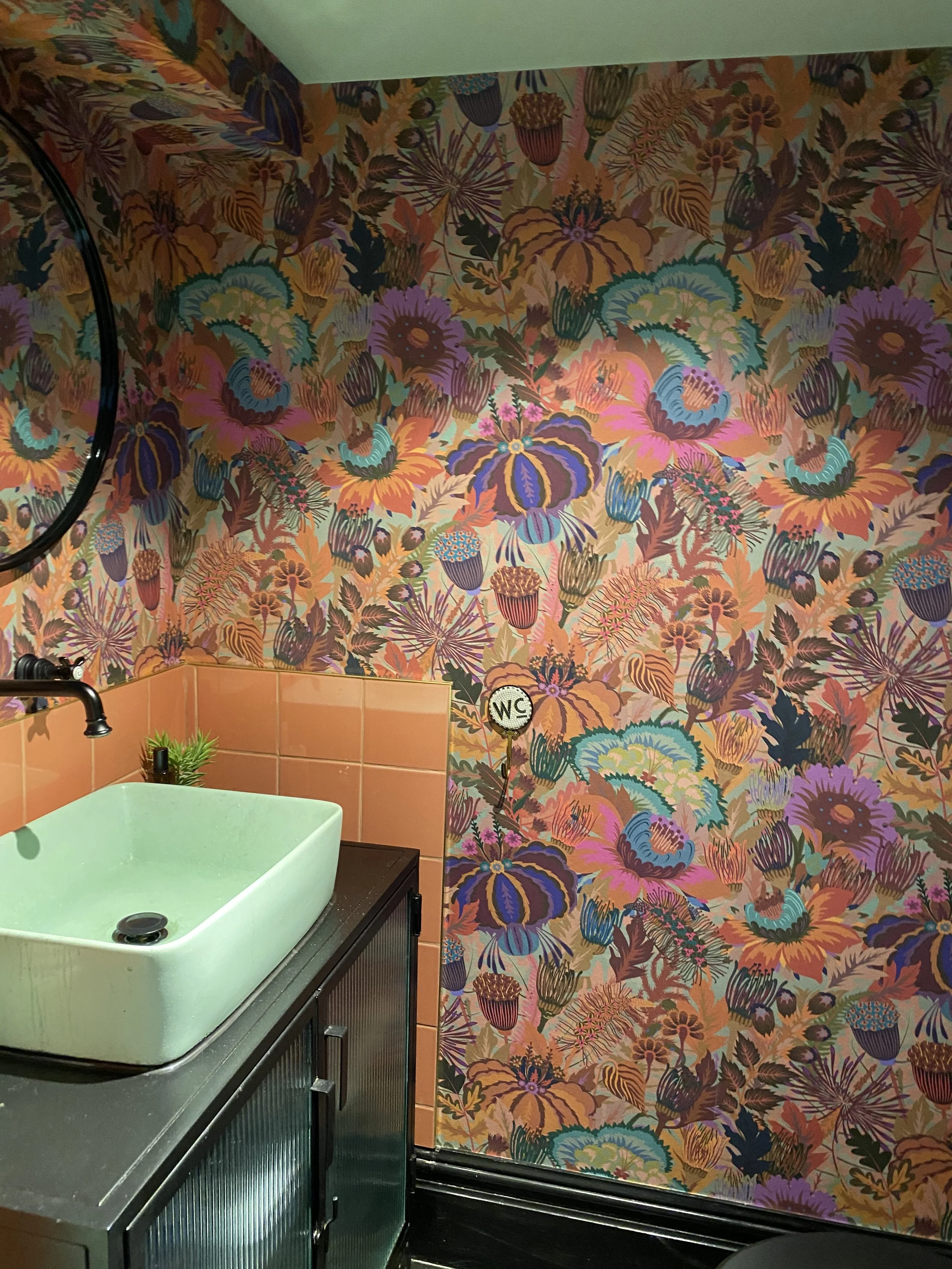 Interior of a bathroom with vibrant floral wallpaper and a mint green sink on a black cabinet.