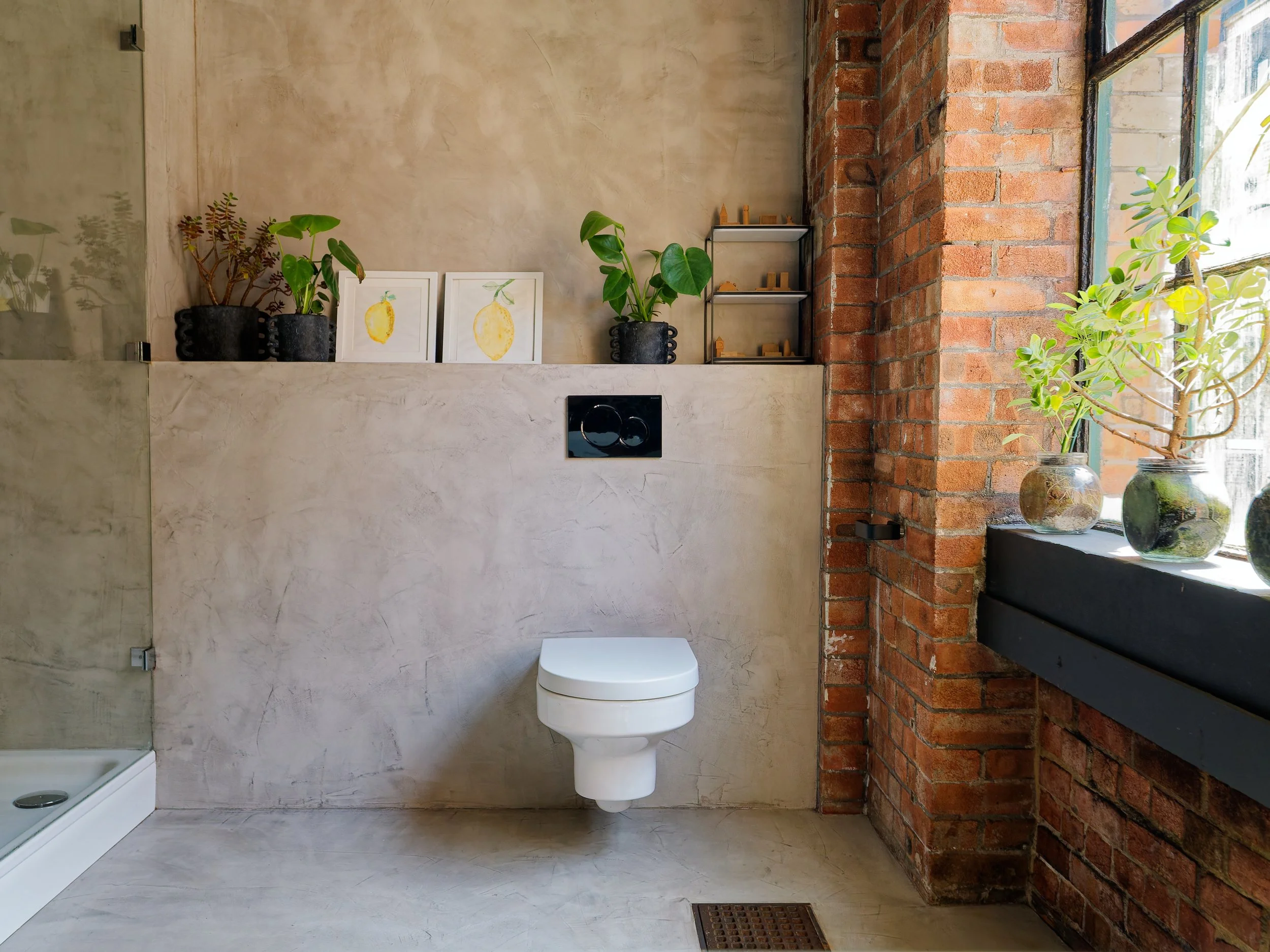 Modern bathroom with beige textured walls, a white wall-mounted toilet, black shelves with potted plants, and a window with three vases and plants.