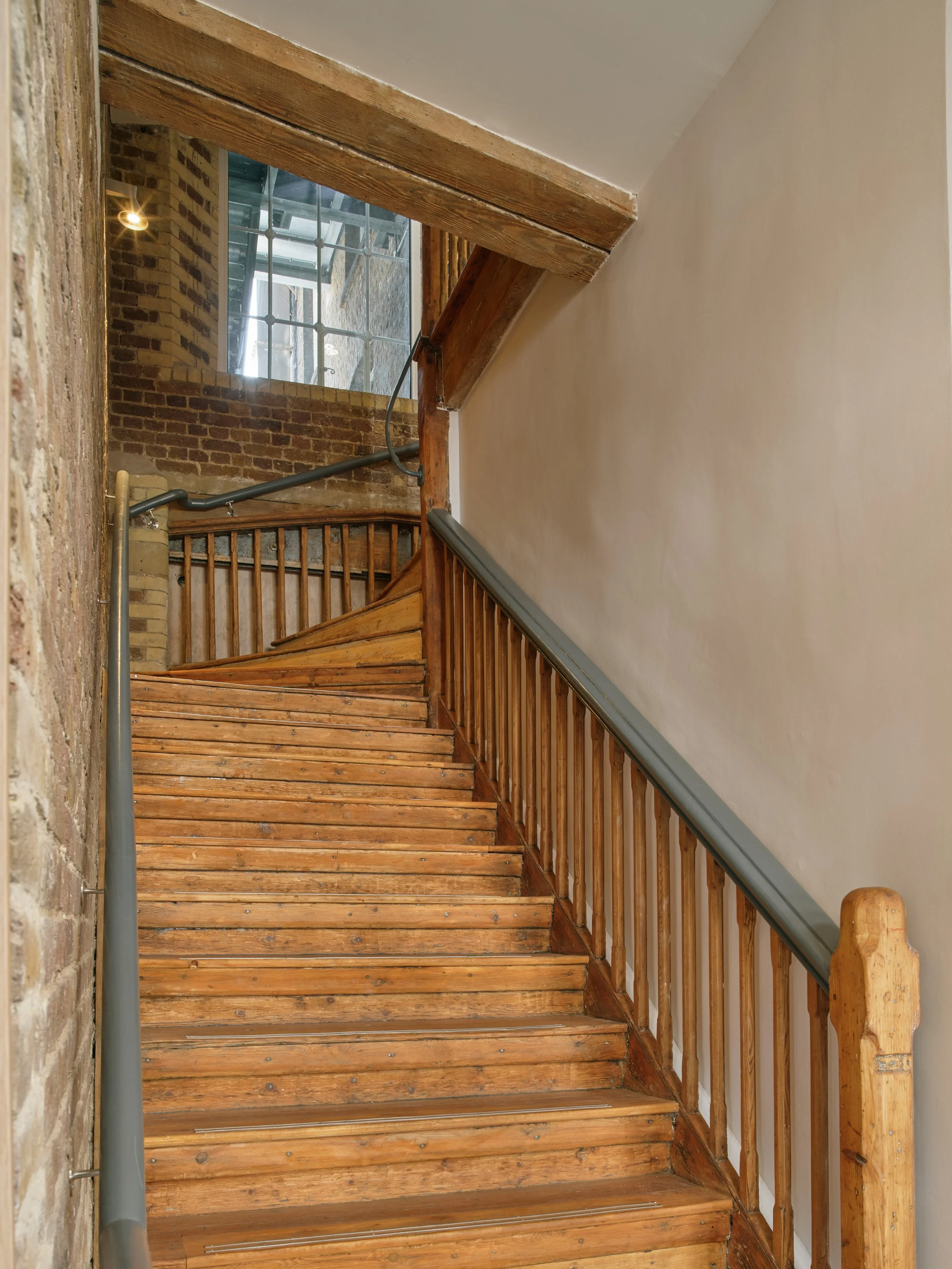 Wooden stairway with railing, brick wall, and window at the top.
