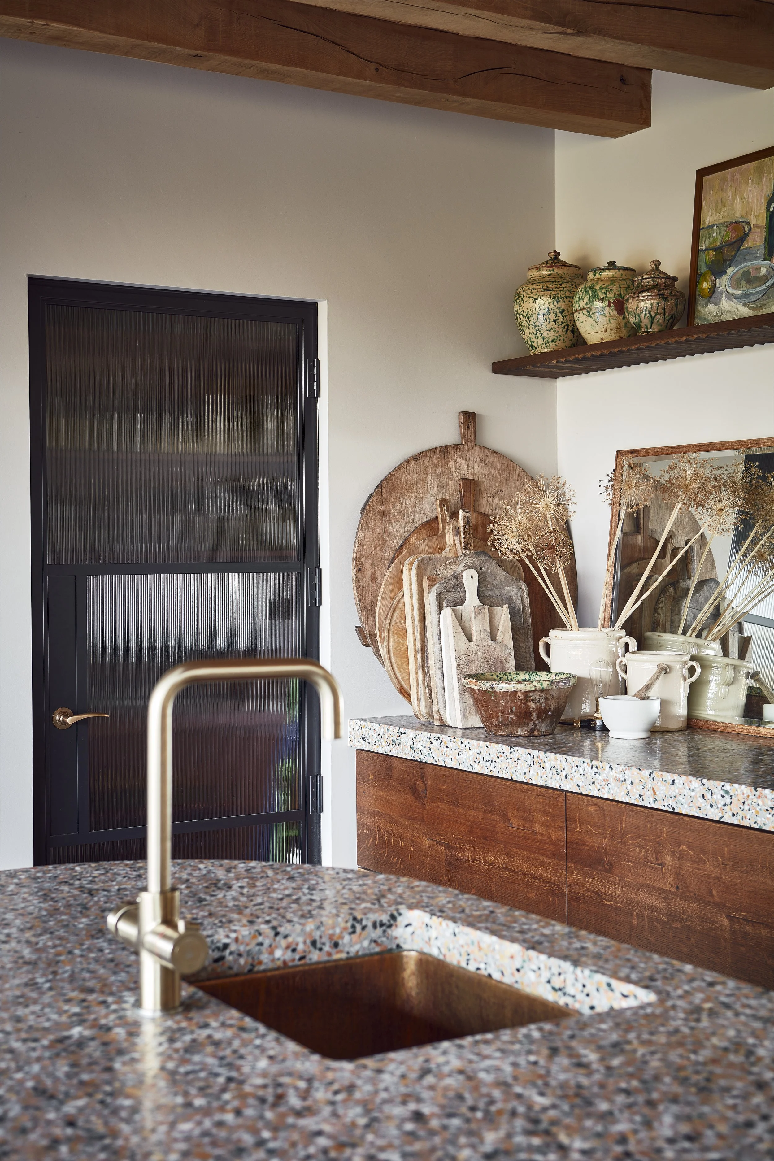 Kitchen with wooden cabinets, a black door with textured glass, a granite countertop, and decorative pottery on wooden shelves.