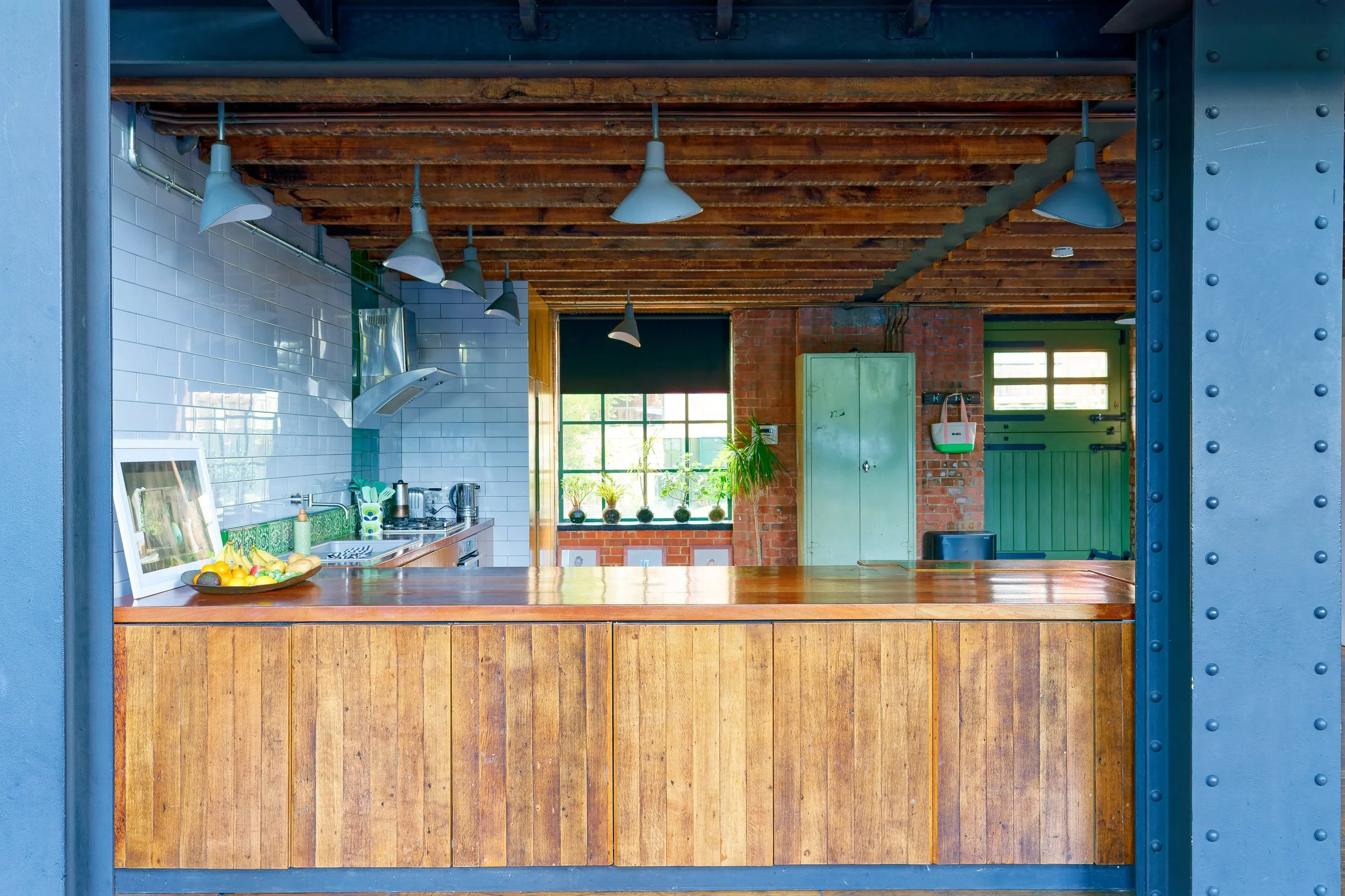A modern kitchen with a wooden breakfast bar, white subway tile backsplash, and visible ceiling beams.