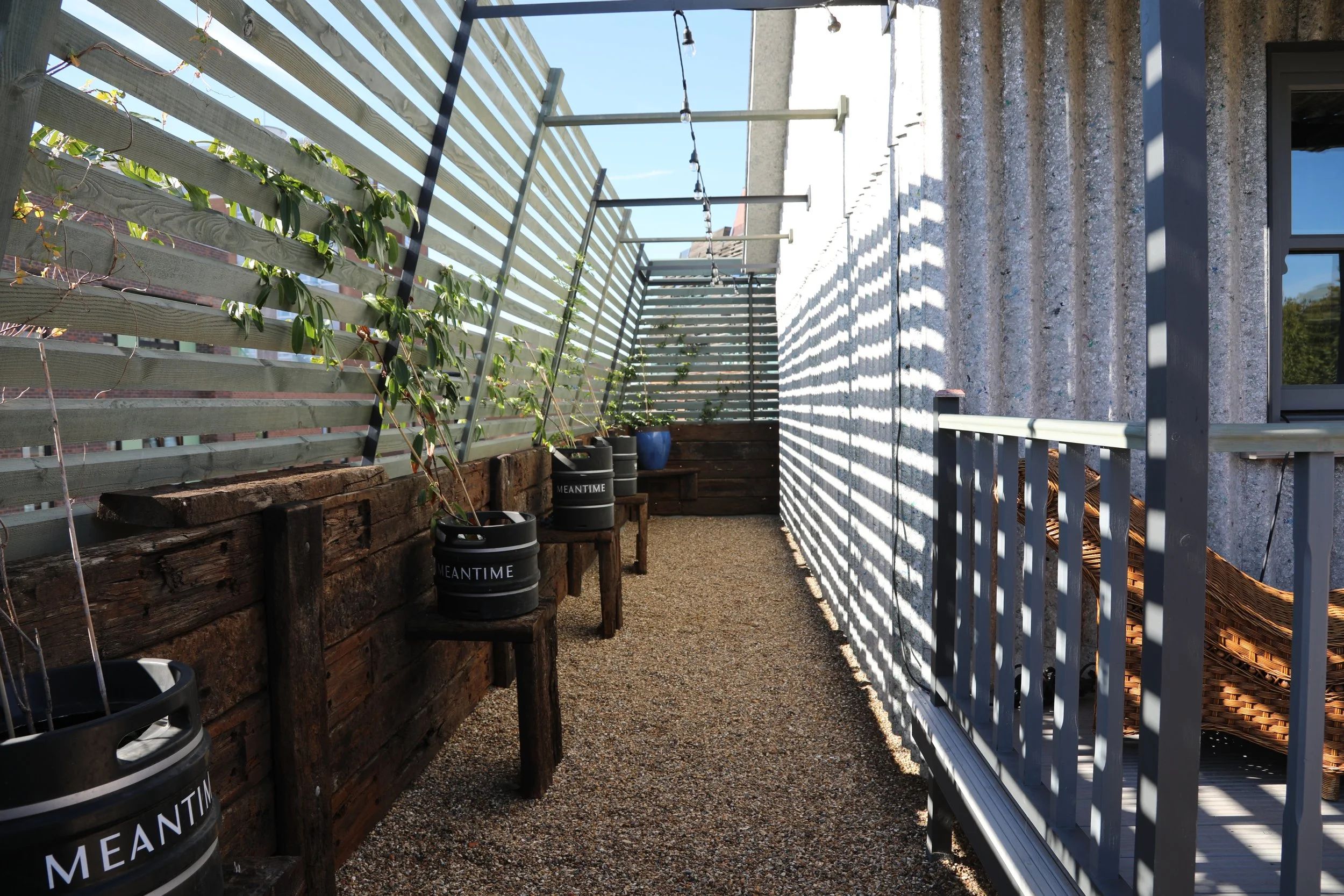 Balcony with potted plants, wooden bench, wooden wall, and a netted privacy screen, with shadows cast from string lights.