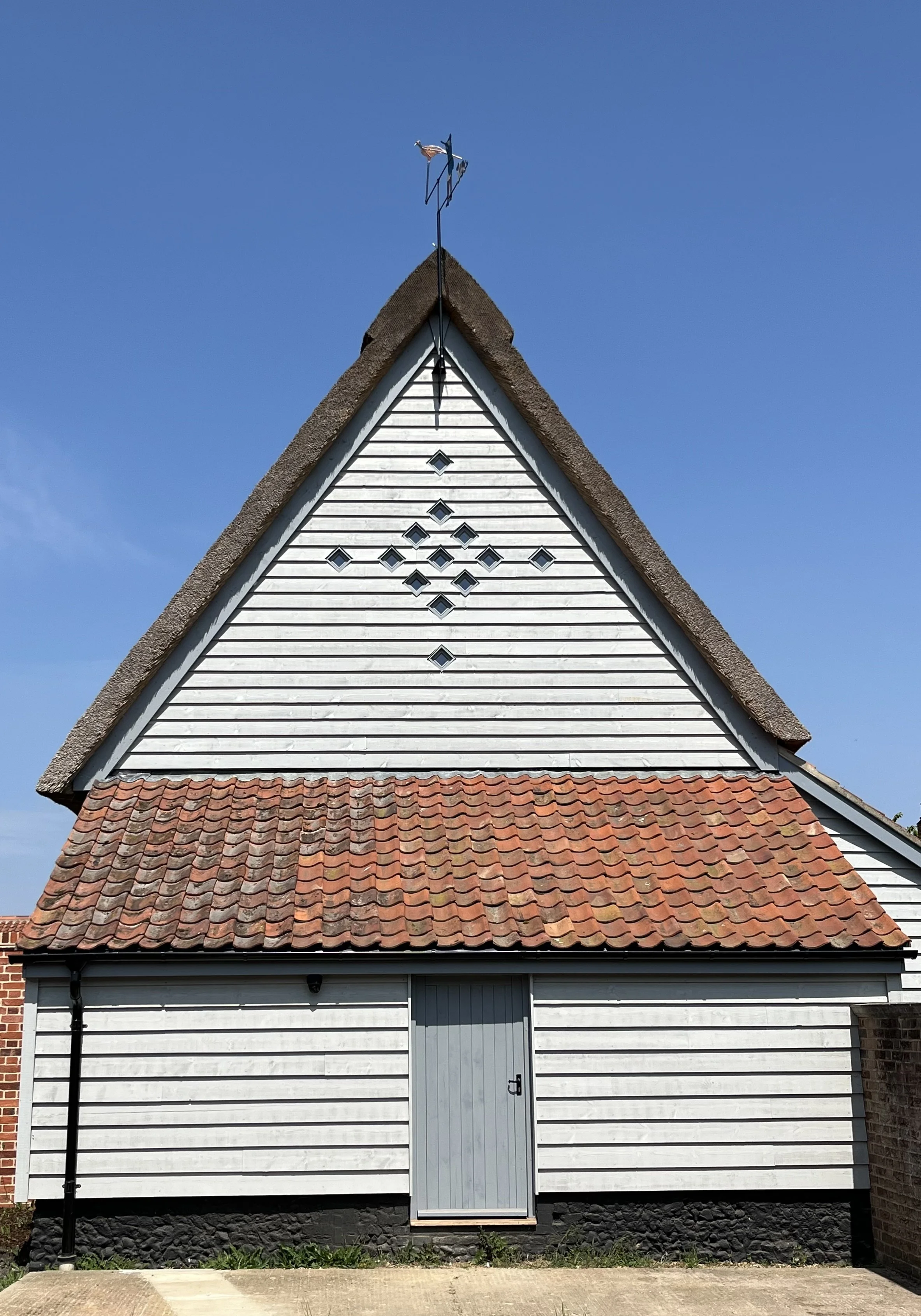 A small historic church with white wooden clapboard siding, a tiled roof, and a steep A-frame roof with a weather vane and small decorative windows.