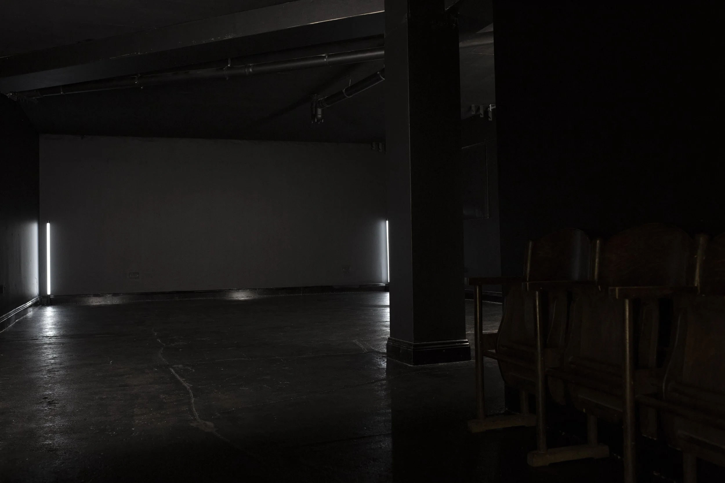Dimly lit theater or auditorium with rows of chairs and faint light coming from the sides.