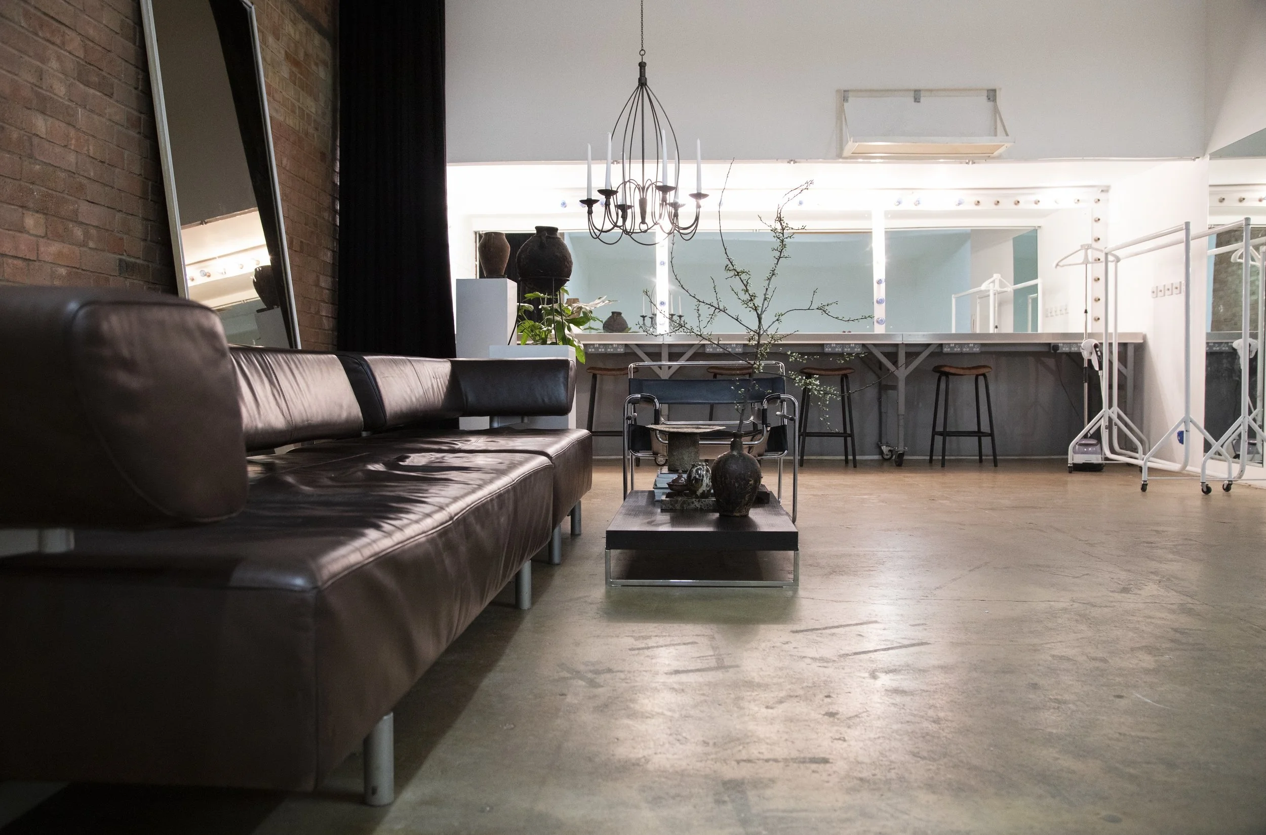 Empty modern living space with a leather sofa, a coffee table with decorative vases, a large mirror, and a bar area with stools in the background.