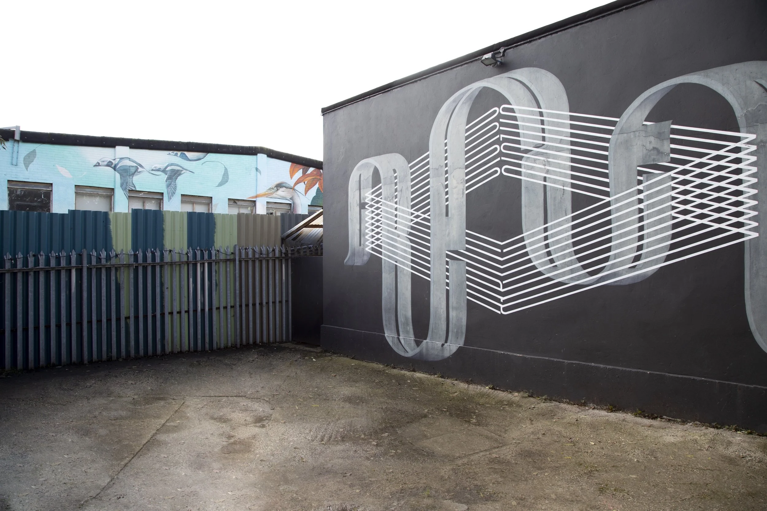 Street mural with the word 'CODE' in large, stylized letters painted on the black building wall, featuring white lines extending from the letters.