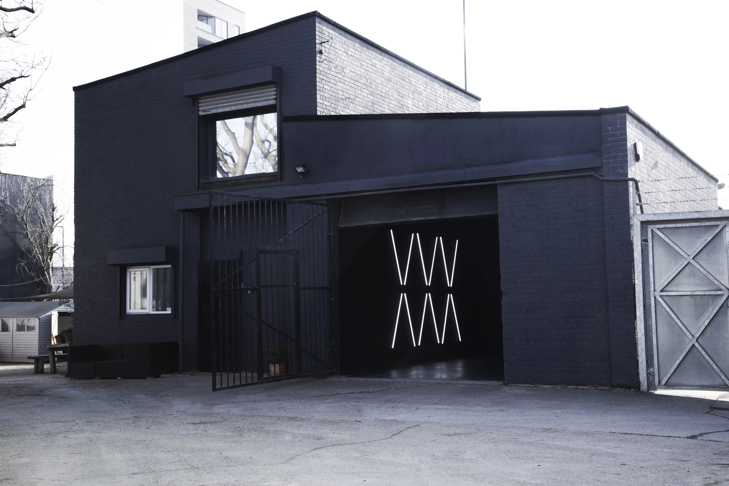 Black building with an open garage door featuring modern LED light art installation, and a window on the upper level.