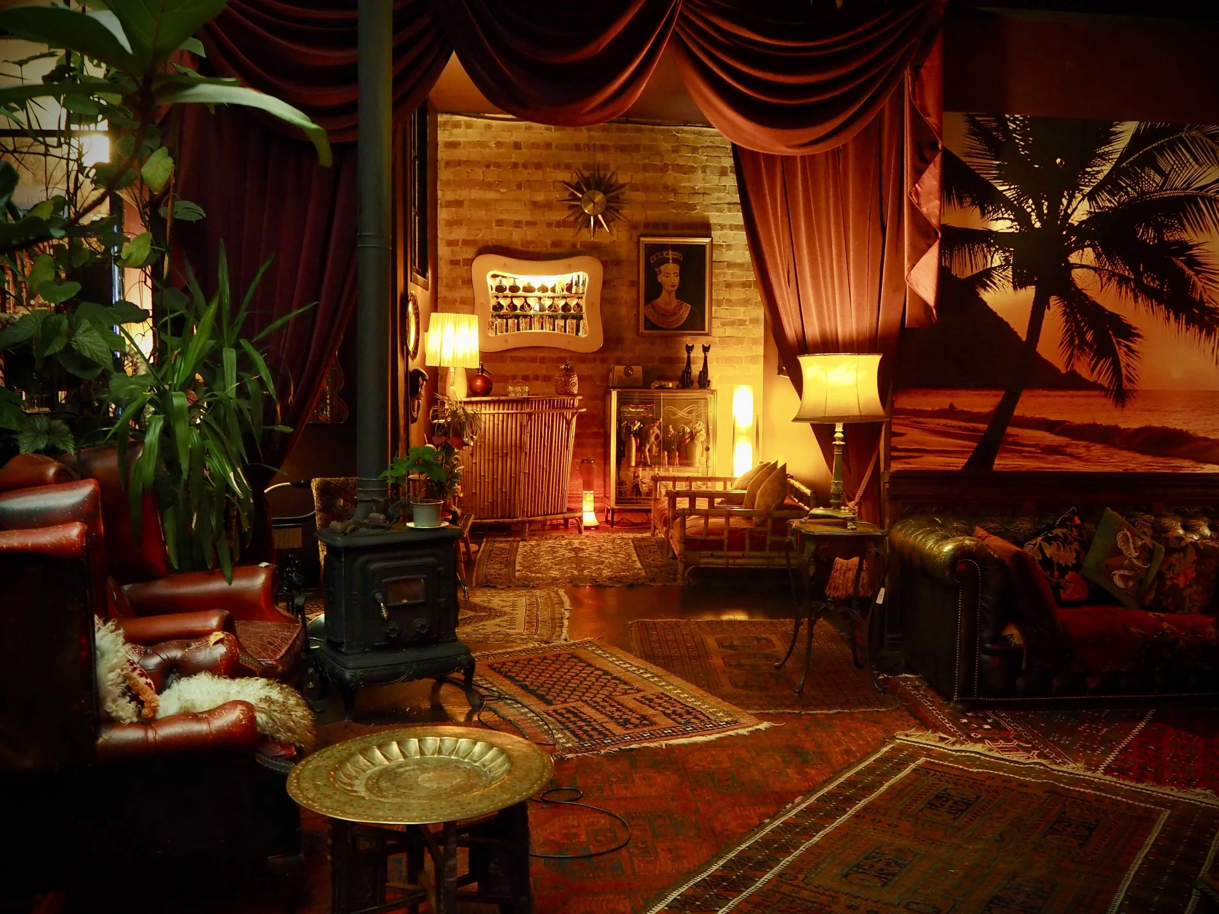 Cozy living room with vintage furniture, colorful rugs, tropical wall mural, and warm lighting.