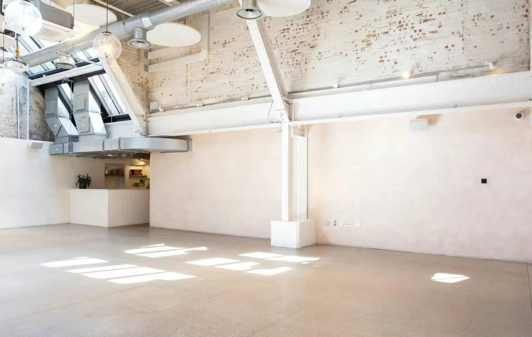 Empty modern industrial-style loft with high ceilings, exposed ductwork, large windows, and minimal decor.