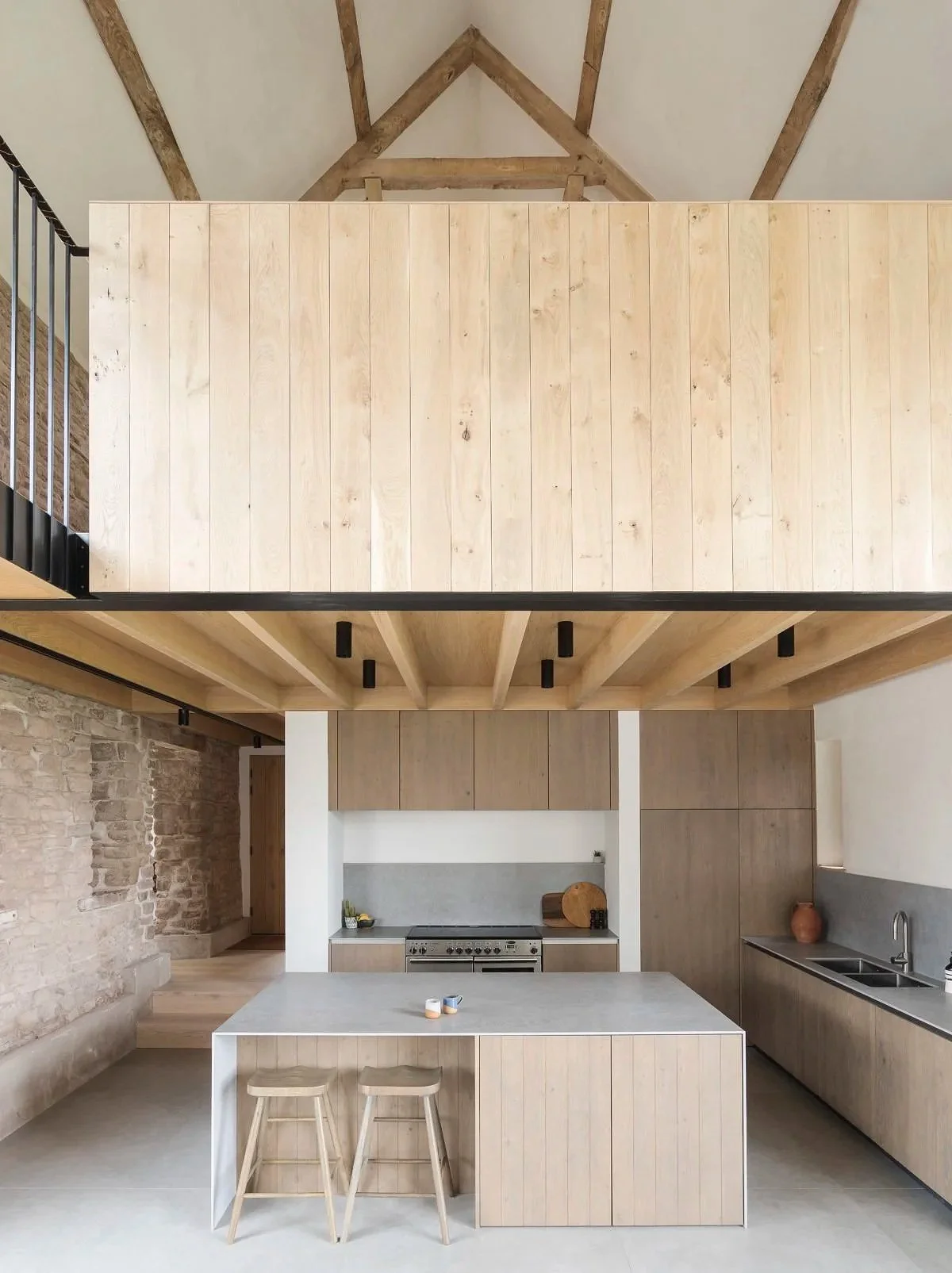 Modern kitchen with wooden cabinets, an island with stools, exposed brick wall, and minimalist decor.