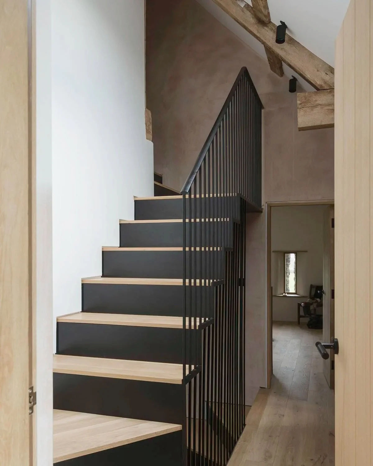 Interior view of a modern staircase with black and natural wood design, leading to the upper floor of a house.