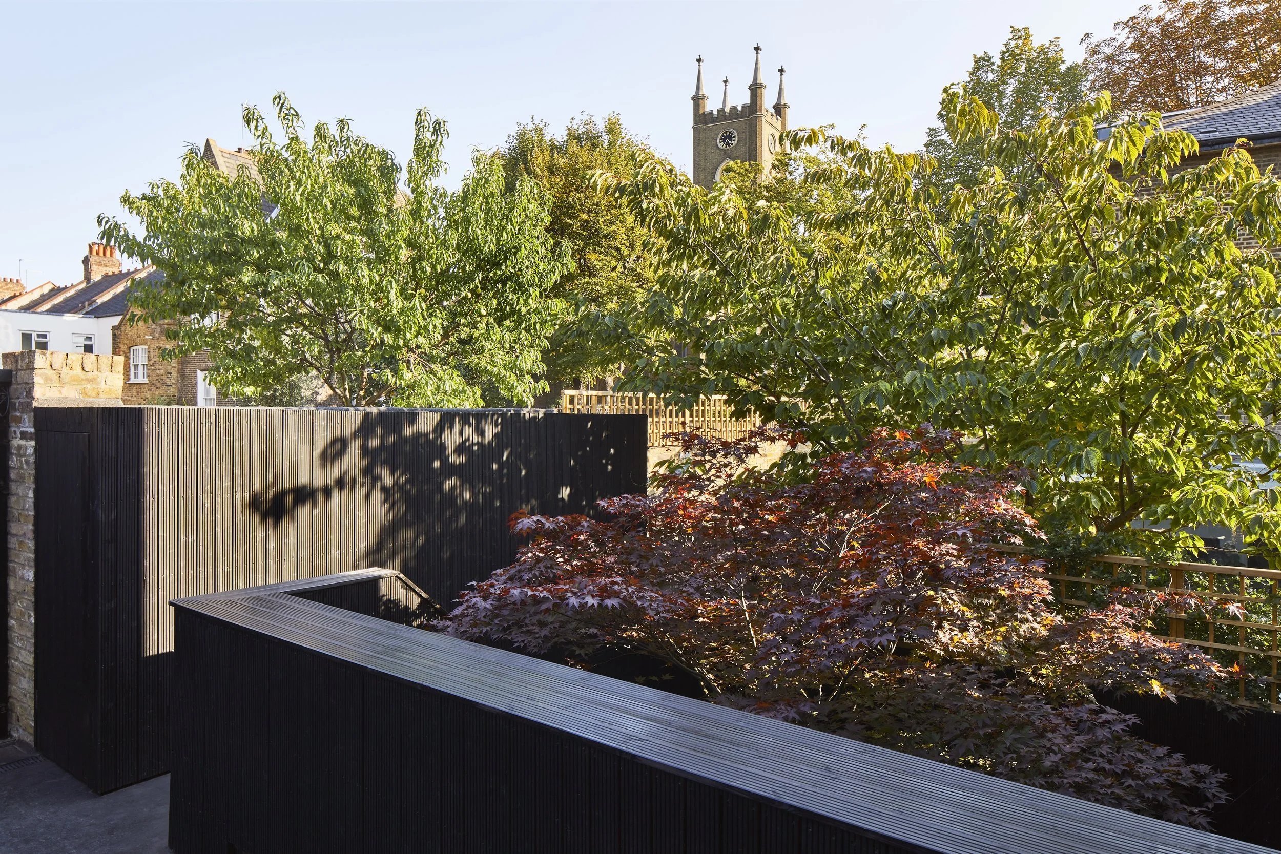 A backyard garden with trees, a black fence, and a church steeple with a clock tower in the background.