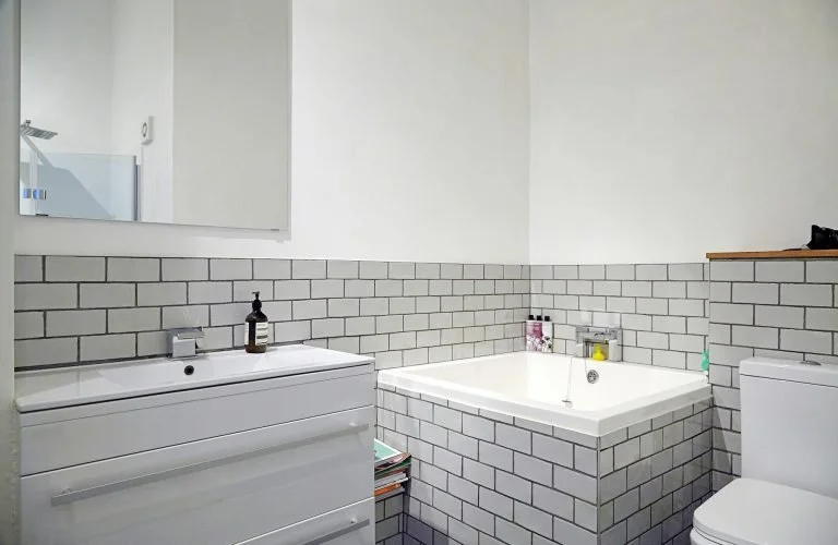Modern bathroom with white vanity, gray subway tile wainscoting, bathtub, and toilet.