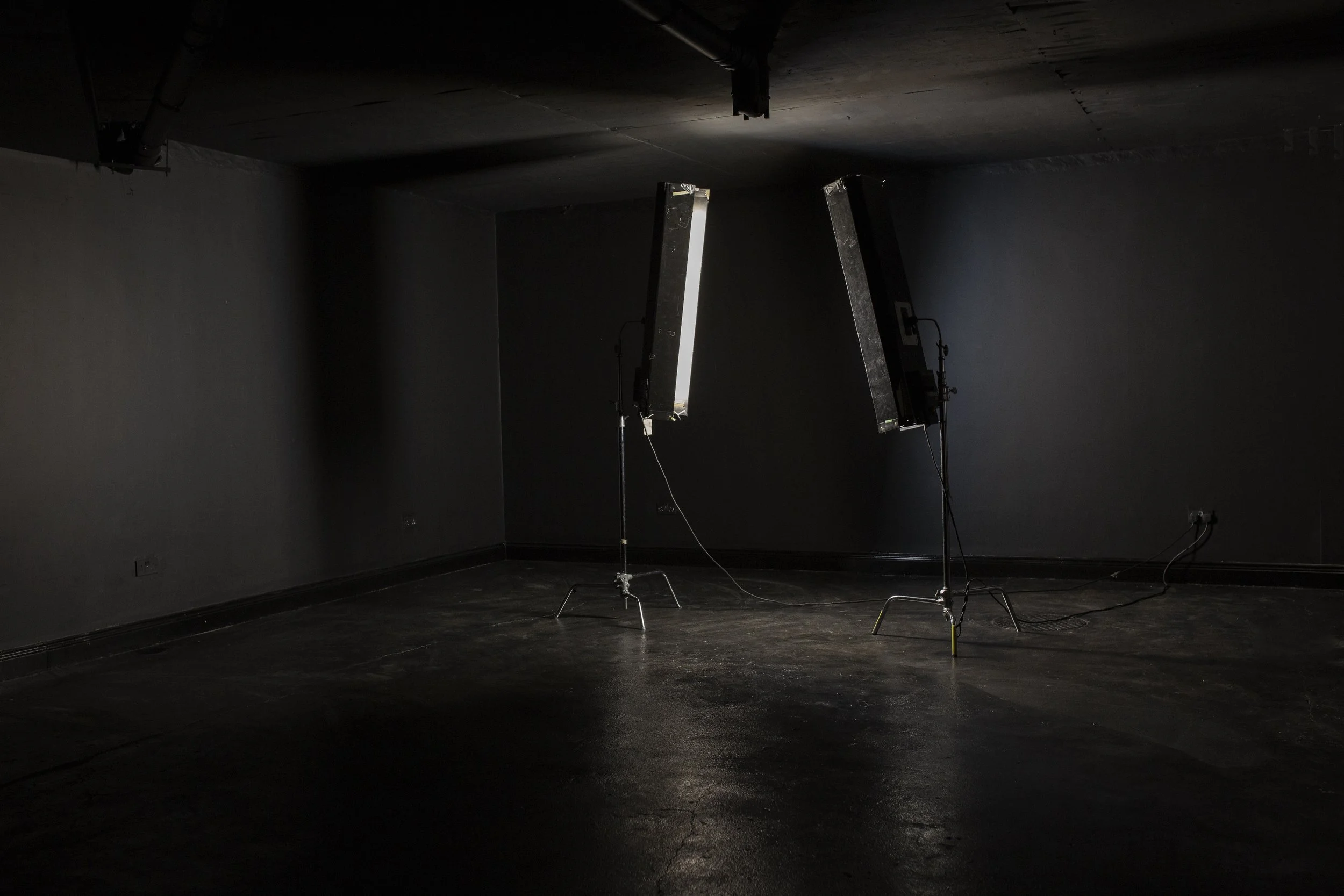 Empty dark room with two studio lights turned off on stands.