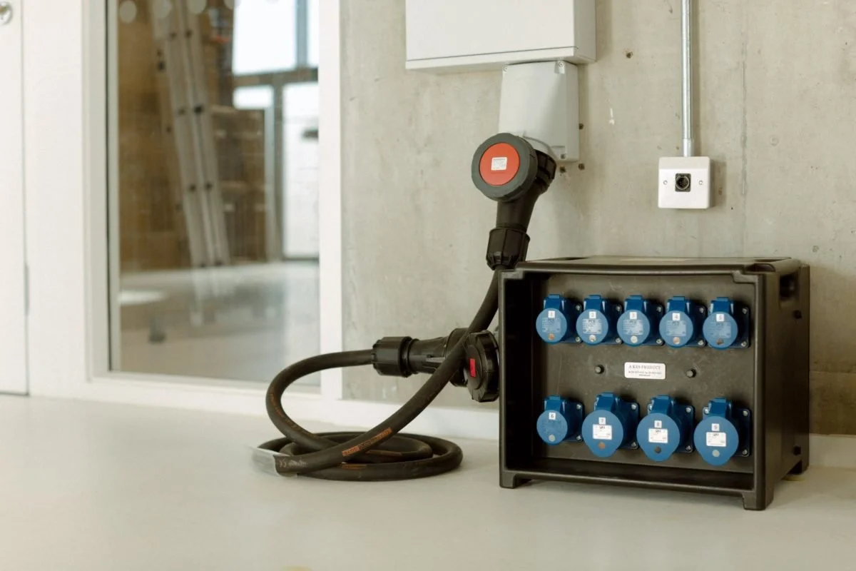 Electrical power strip with multiple blue outlets, connected to an extension cord and mounted on a concrete wall with a nearby electrical outlet.