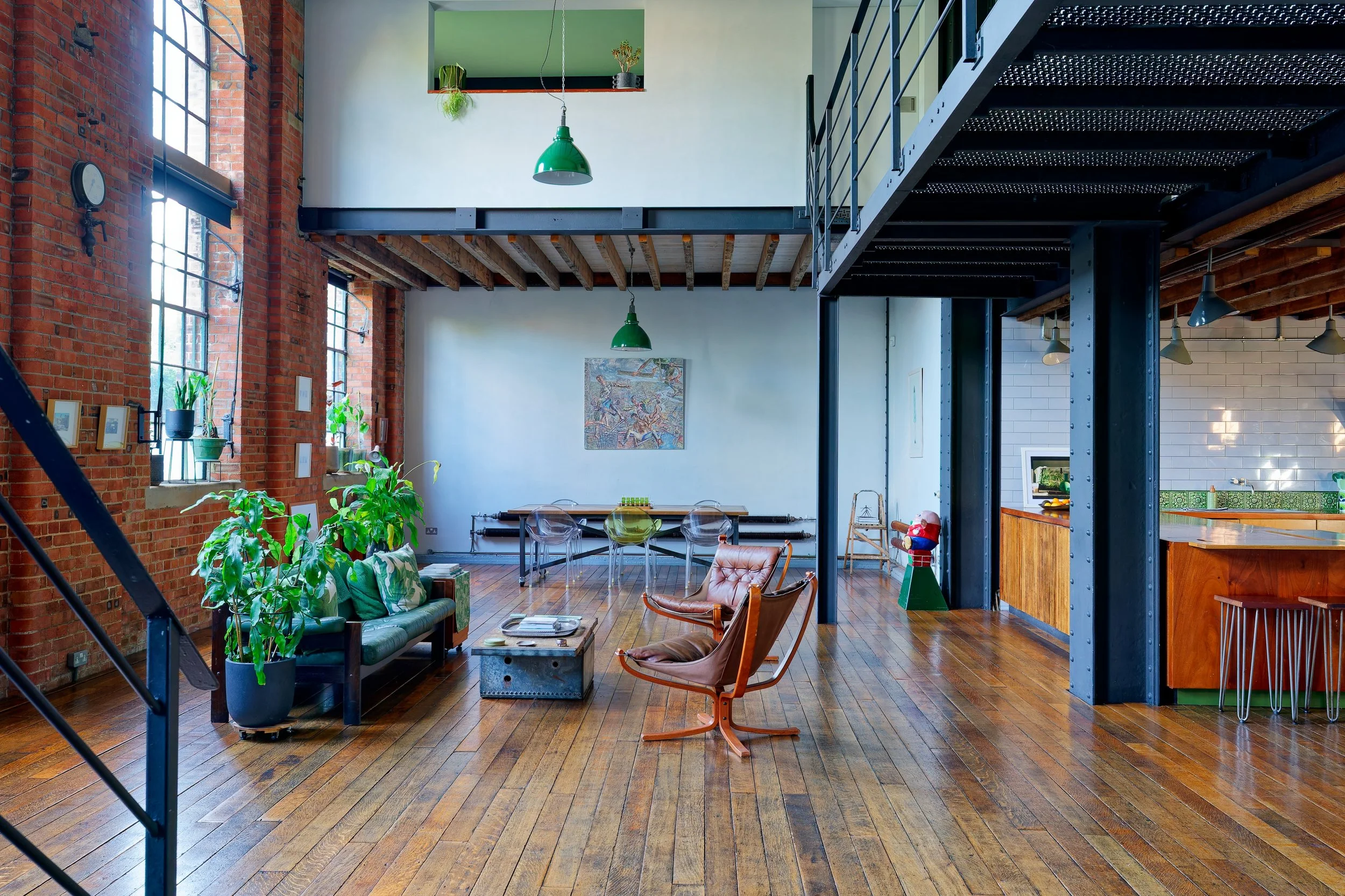 Spacious loft apartment with brick walls, large windows, wooden floors, and modern furniture, including a sofa, chairs, and plants.