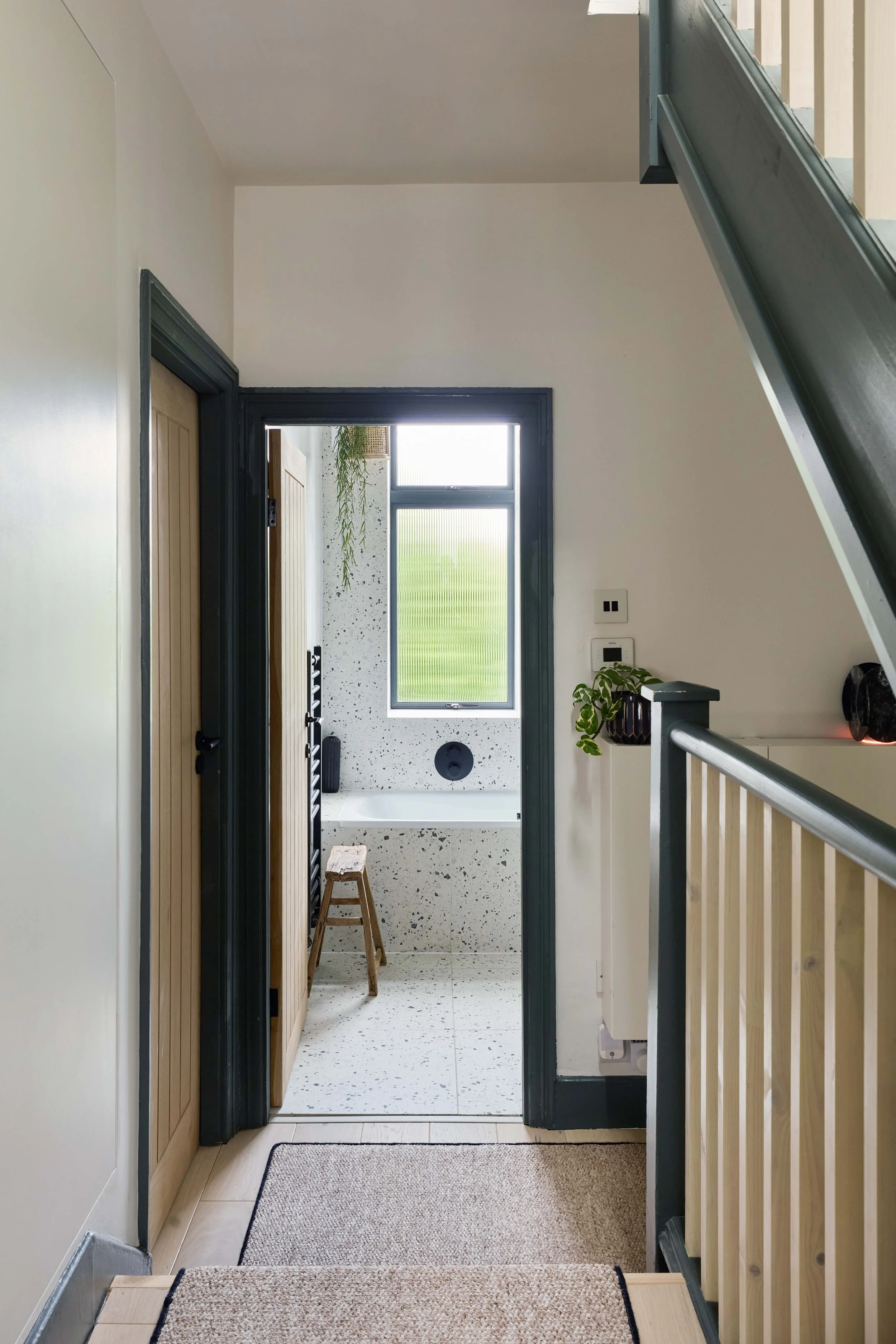 View of a bathroom from the hallway, with a window, a bathtub, and a wooden stool inside.