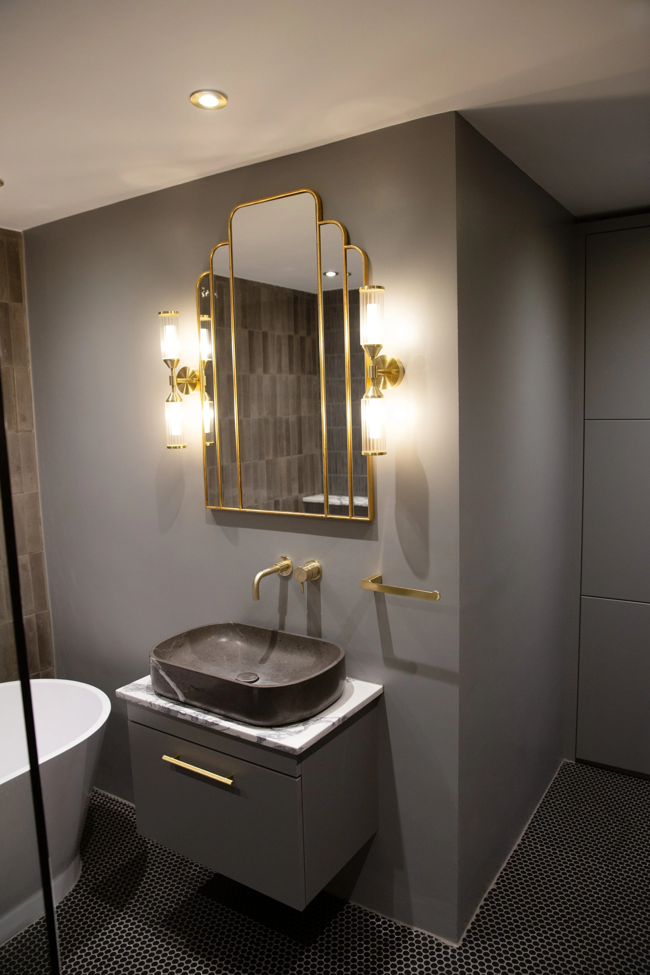 Modern bathroom with gray walls, black stone sink, gold fixtures, and a decorative mirror with lighting.