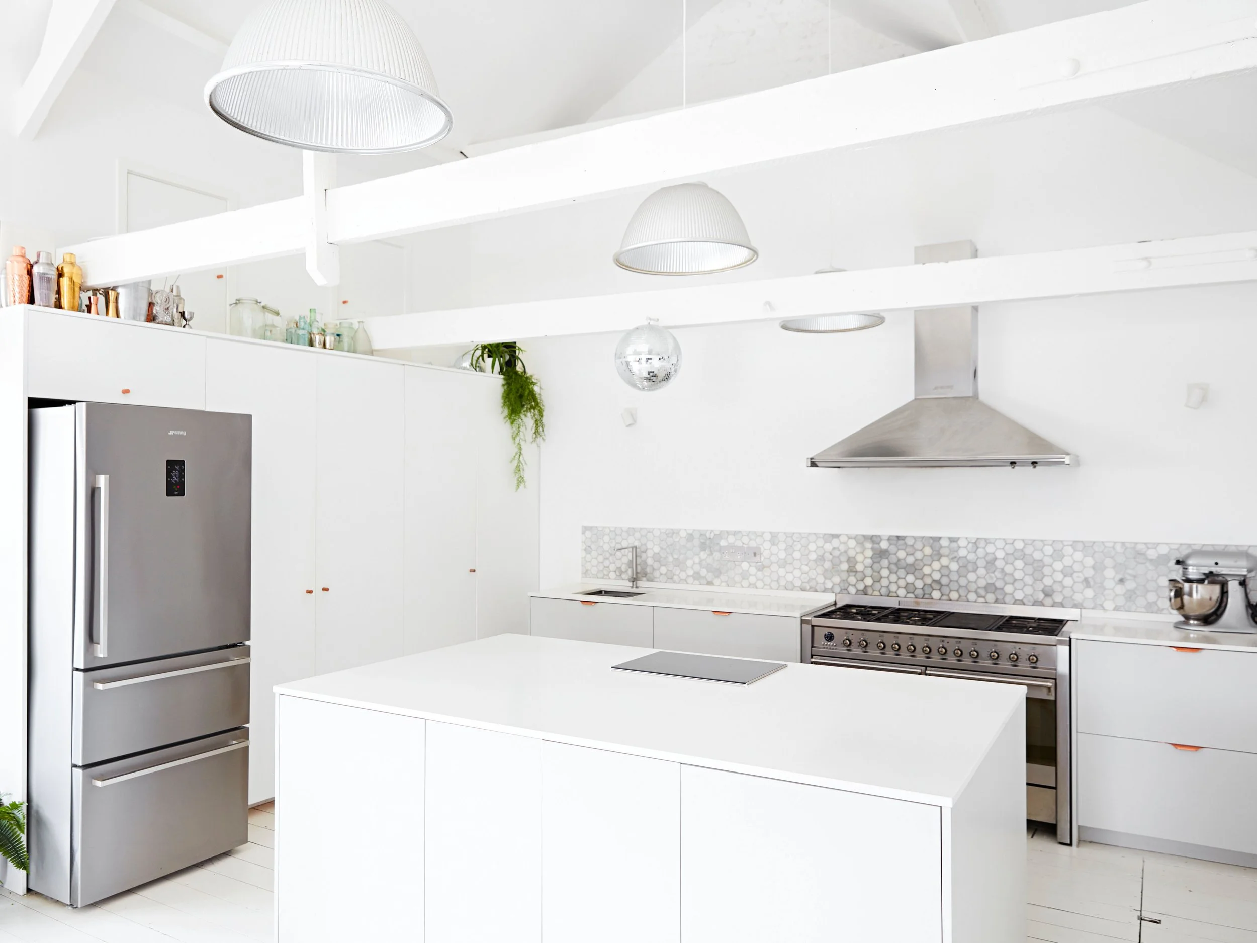 Modern white kitchen with stainless steel appliances, including a refrigerator and oven, minimalist cabinetry, a kitchen island, and pendant lighting.