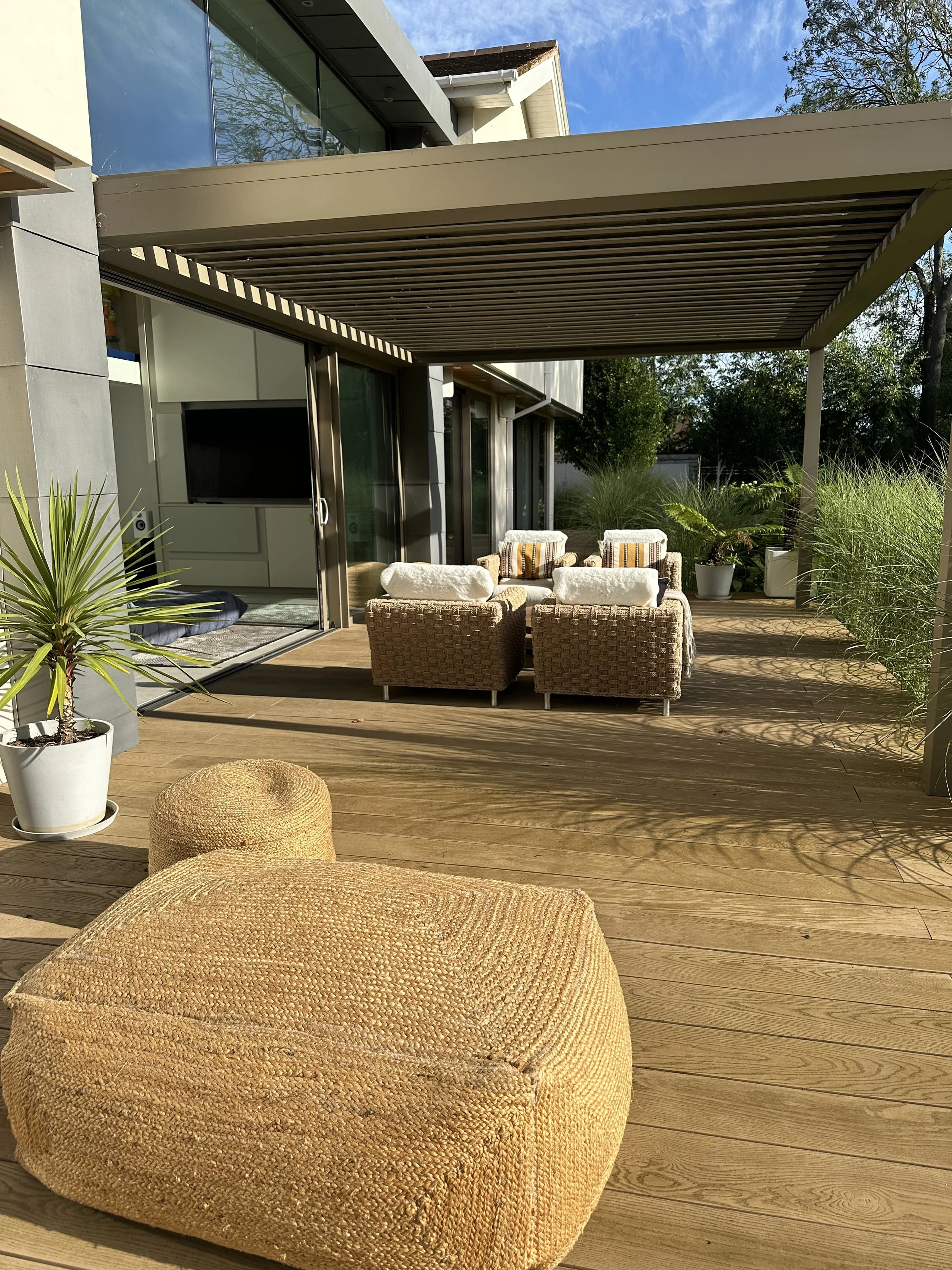 Outdoor patio with wicker and fabric lounge chairs, potted plants, and a retractable awning on a sunny day.