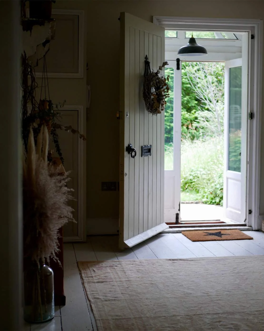 Open front door of a house showing a view of lush greenery outside, with a doormat featuring a star design on the porch.