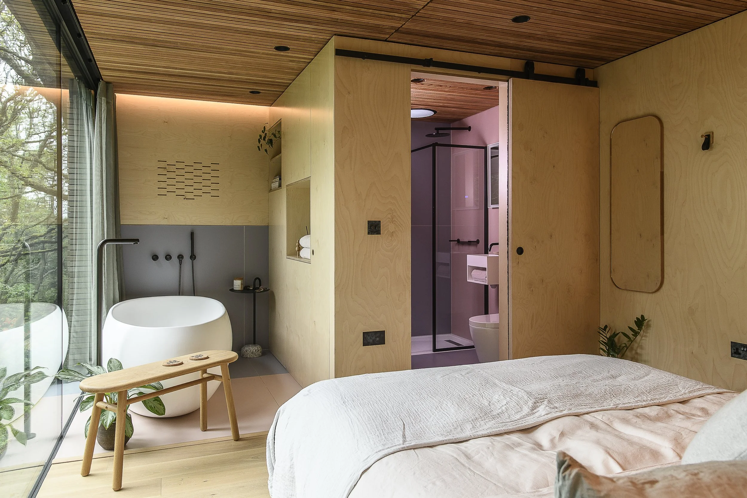 Modern bedroom with a wooden ceiling, large windows, and an open bathroom with a shower and toilet visible.