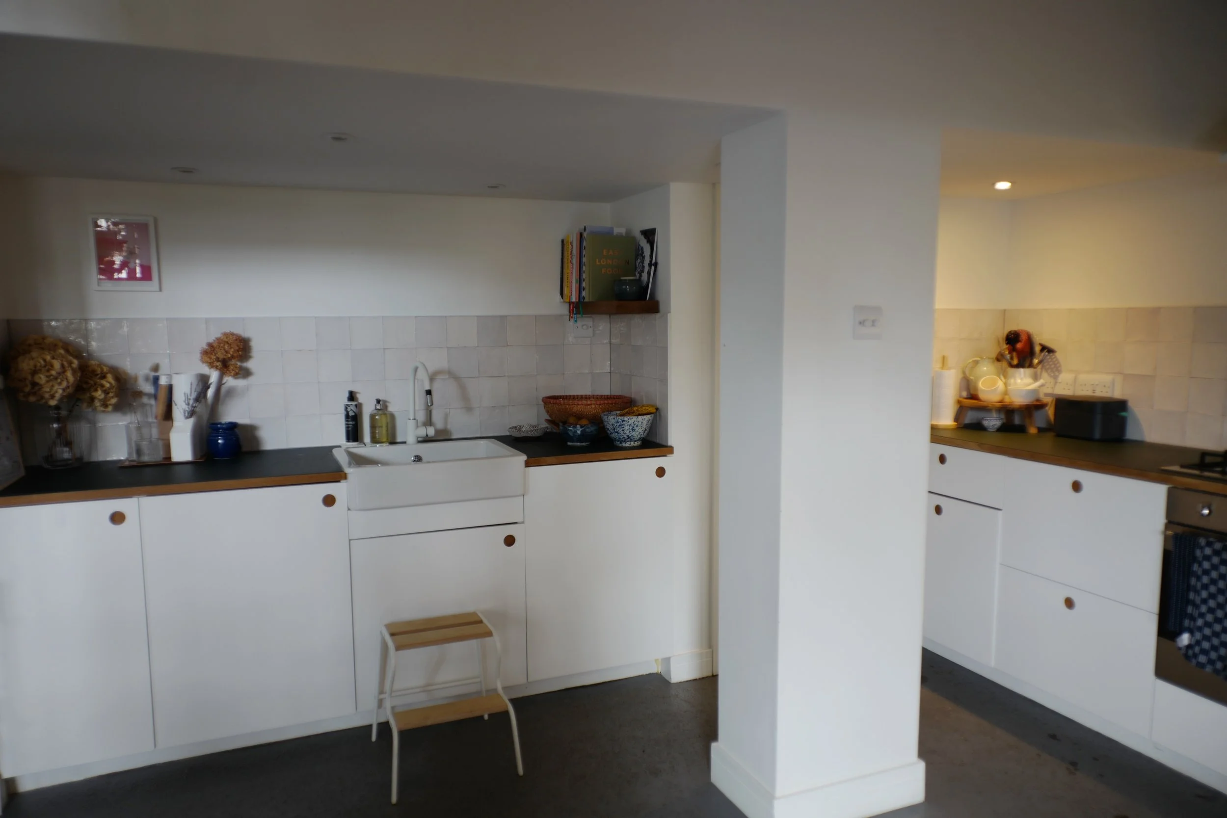 Modern kitchen with white cabinets, black countertops, a farmhouse sink, and decorative bowls and dried flowers on the counter.