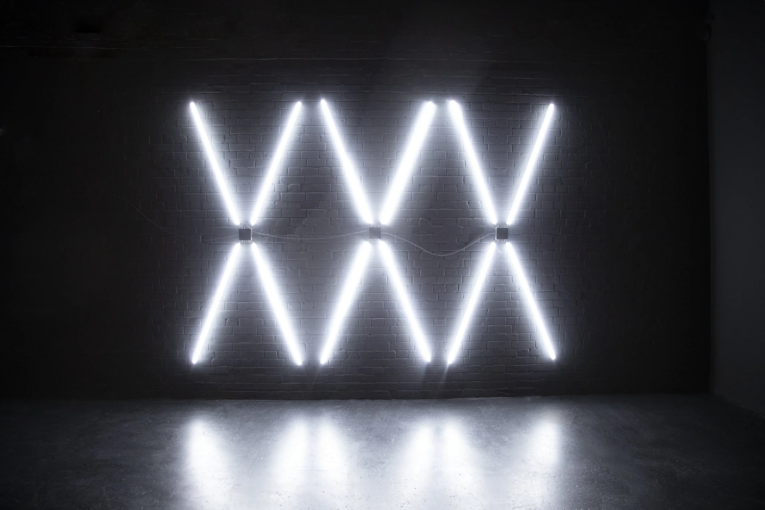 Wall decorated with a pattern of bright white LED lights in a zigzag formation against a dark brick wall.
