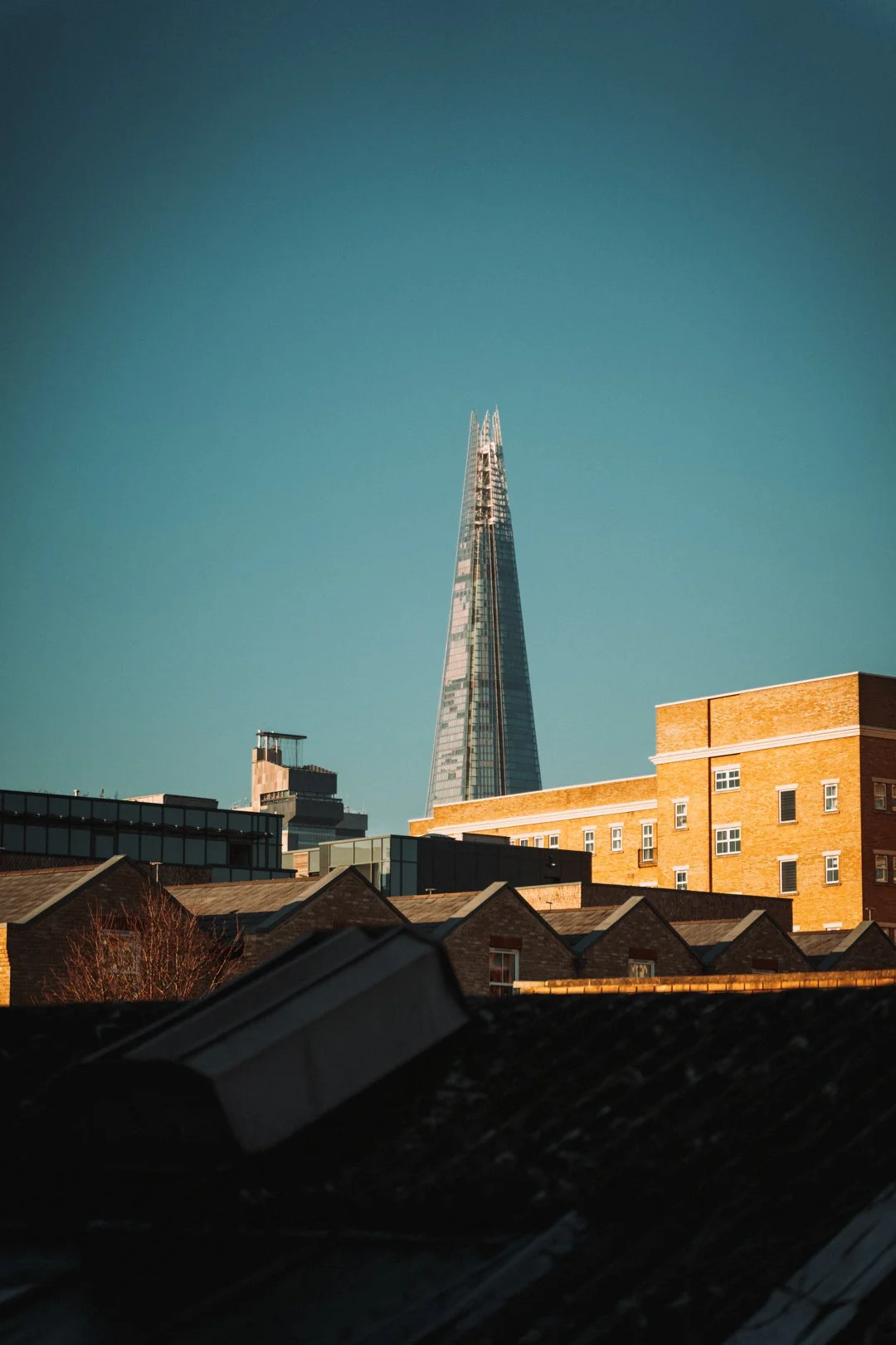 The Shard skyscraper towering over other urban buildings against a clear blue sky.