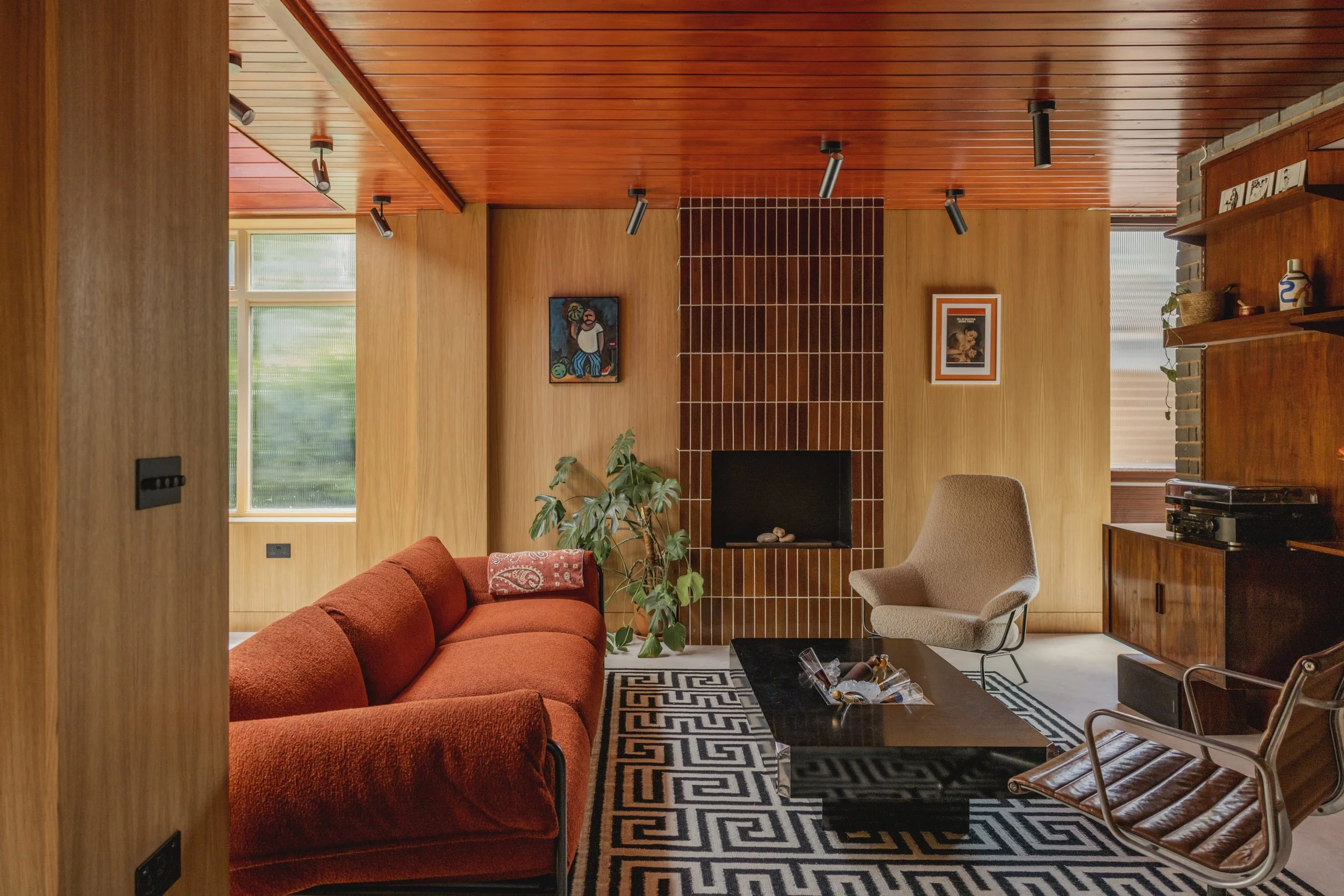 Living room with a red couch, beige armchair, patterned rug, potted plant, fireplace, and wooden walls and ceiling.