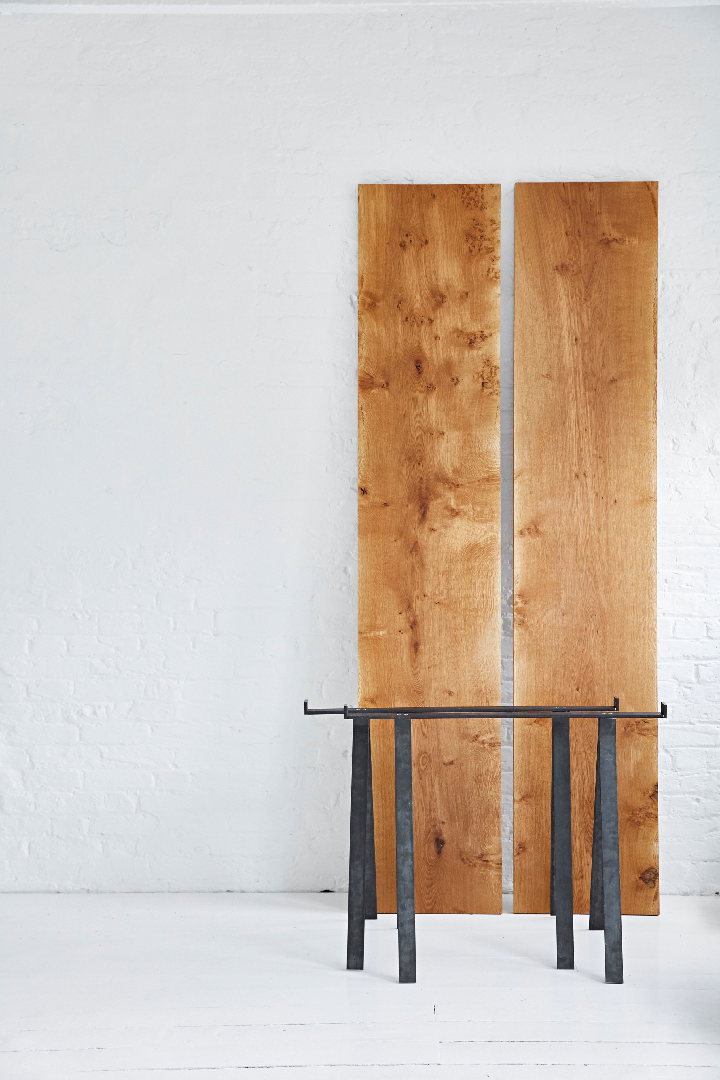 A minimalist interior with two wooden panels leaning against a white brick wall and a black metal table in front of them.