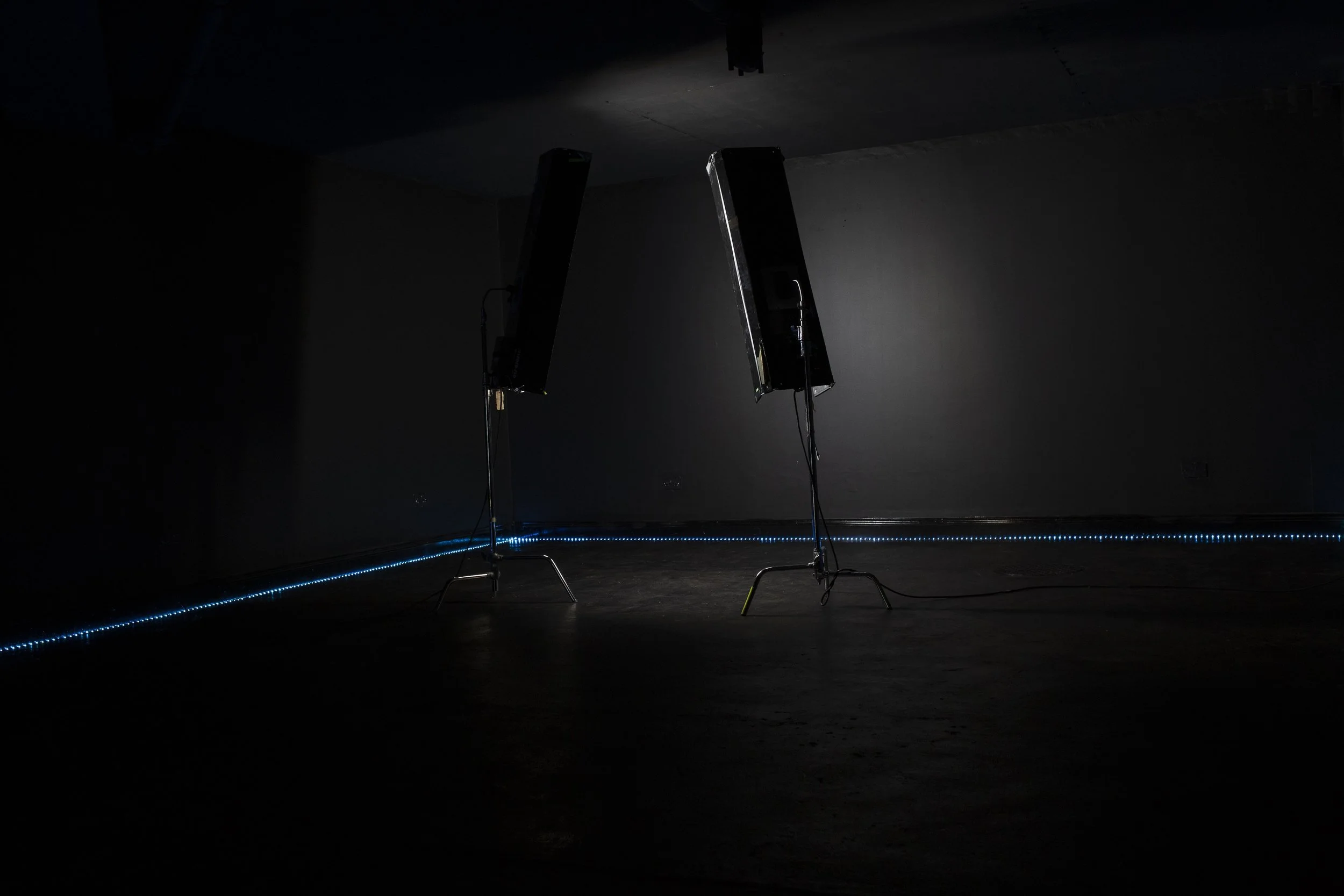 Two large photography or lighting reflectors on stands in a dark room, with a strip of blue LED lights along the floor, and a dark wall and ceiling.