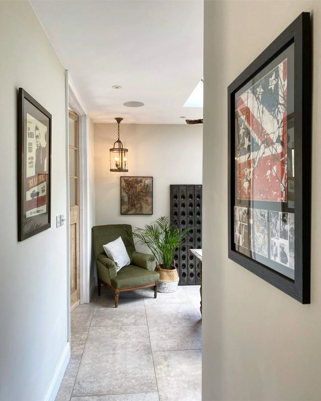 A cozy corner with a green armchair, potted plant, wall art, pendant light, and framed posters.