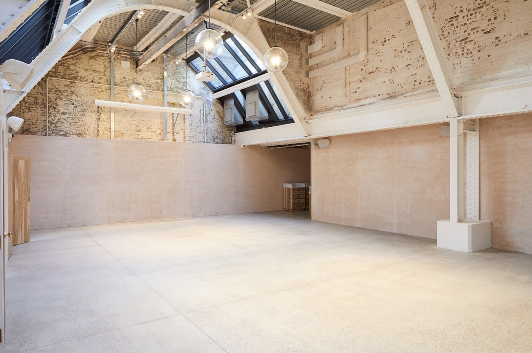 Empty industrial-style event or studio space with high ceilings, exposed brick walls, and large windows letting in natural light.