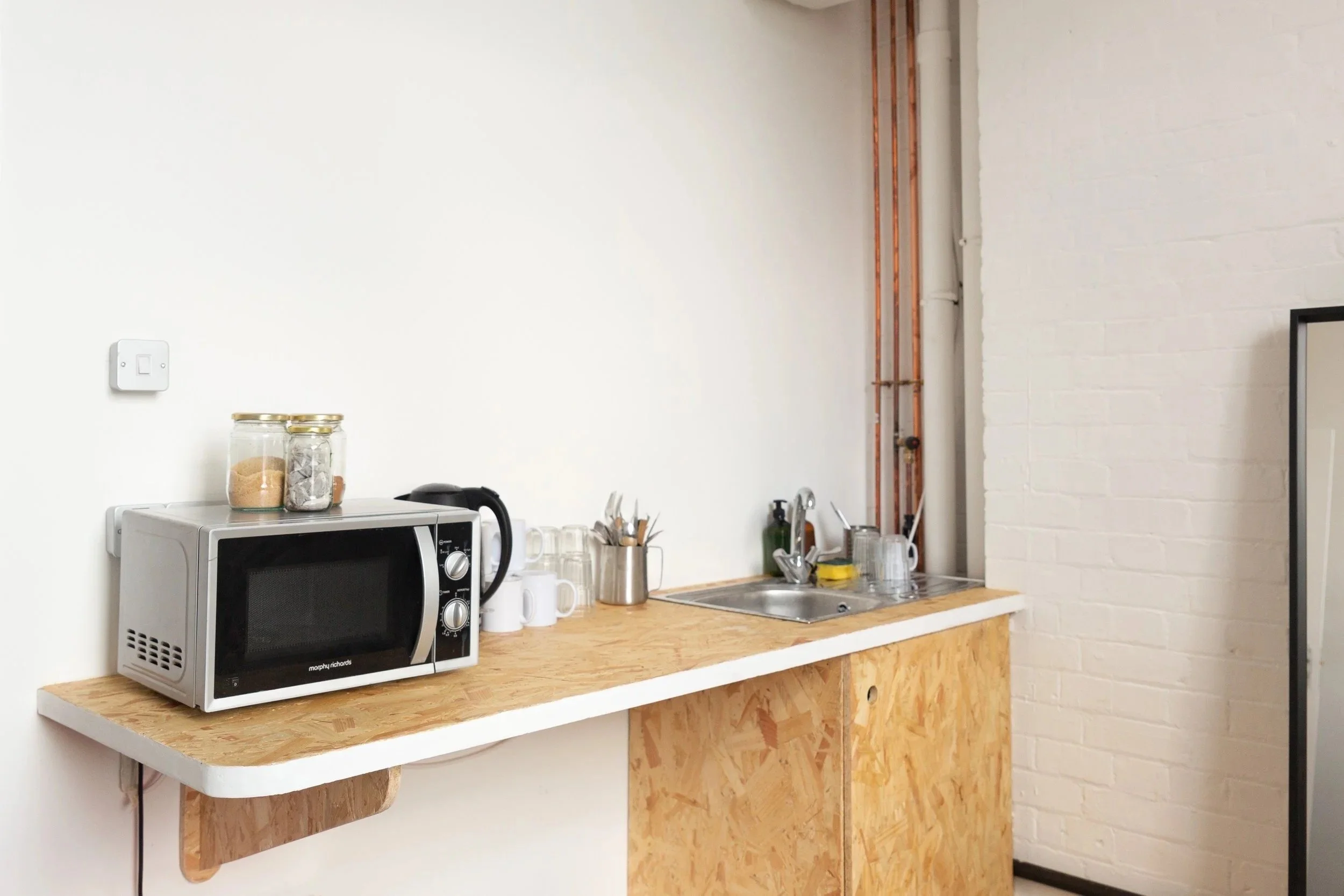 Countertop with microwave, jars, glasses, utensils, and a sink in an industrial-style kitchen.