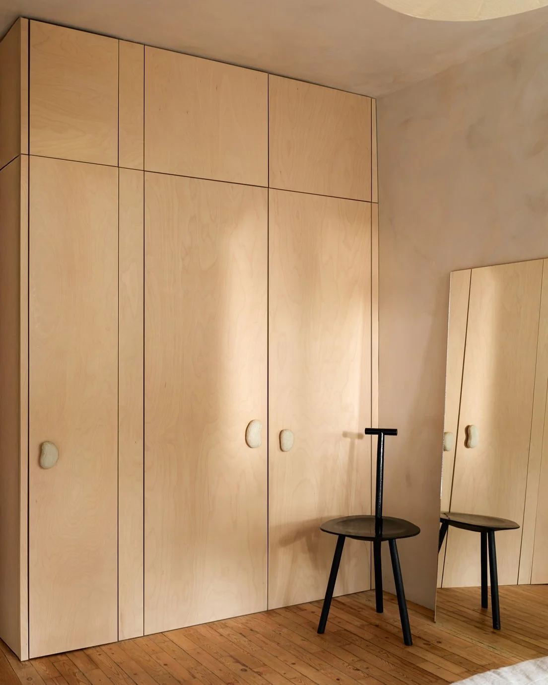 Room with large light wood wardrobe and a small black stool with a mirror leaning against the wardrobe
