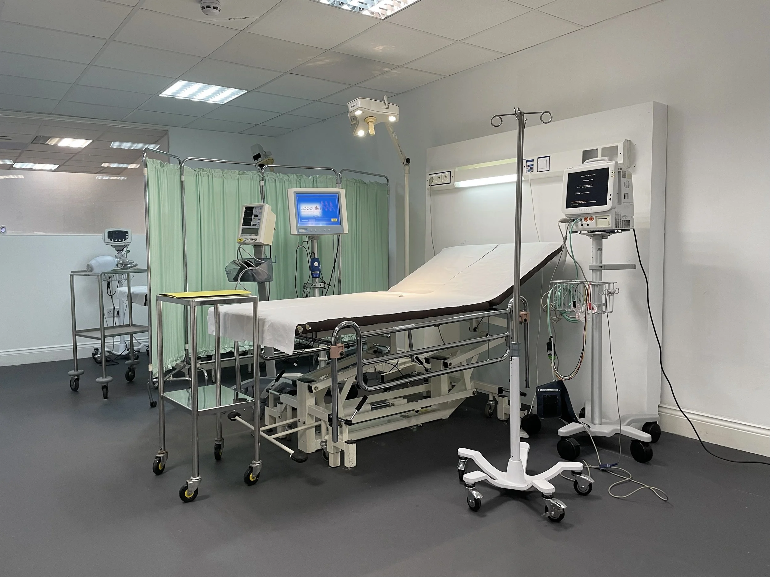 Empty hospital bed with medical equipment including monitors, IV stand, and privacy curtain in a clinical setting