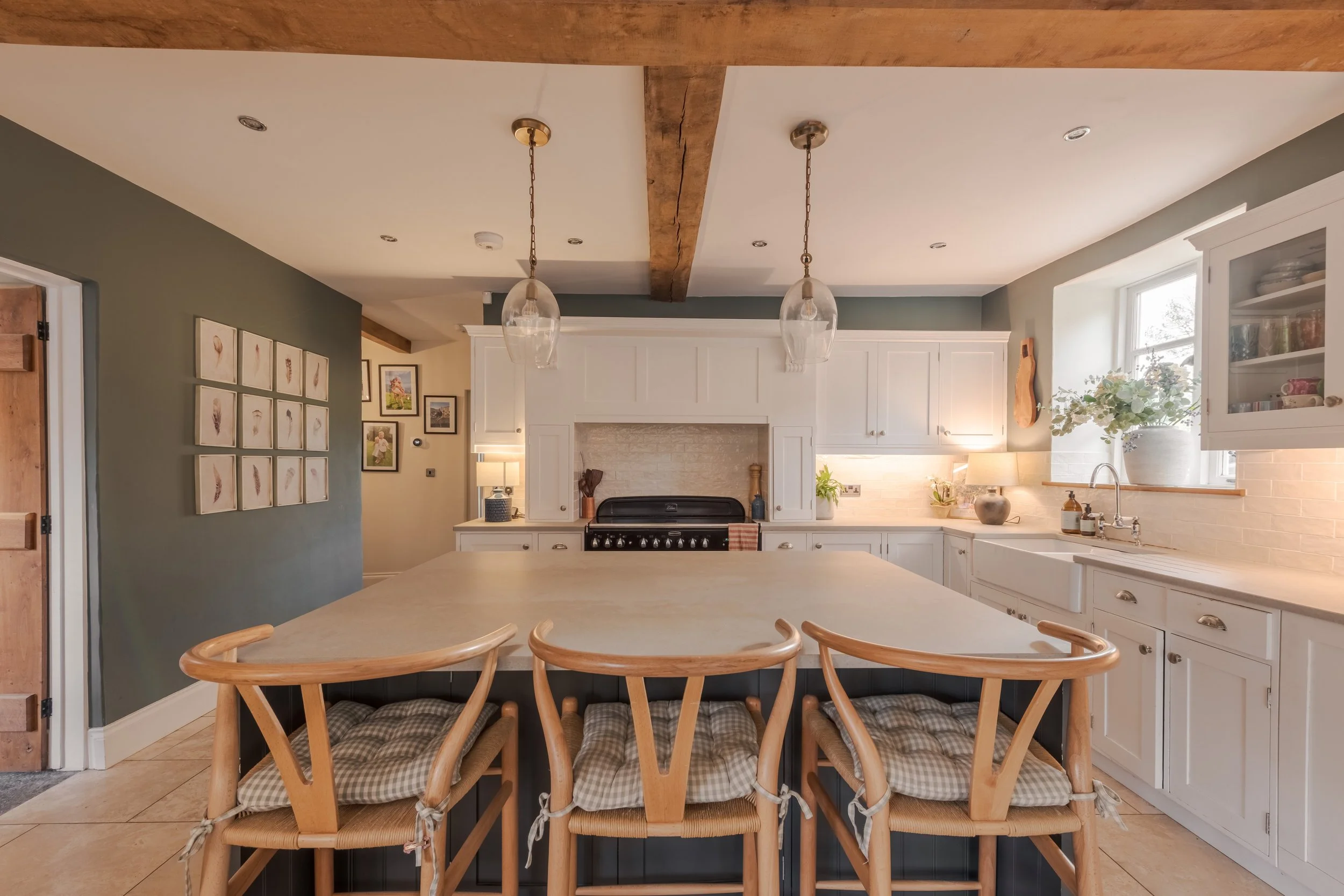 Modern kitchen with white cabinets, a large central island with seating, pendant lights, a black stove, and a window with a vase of flowers.