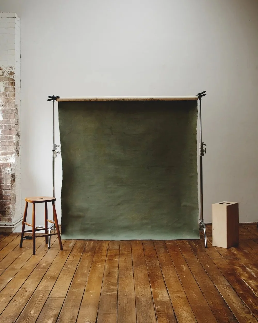 Indoor studio setup with a green backdrop, wooden floor, stool on the left, and a box on the right.