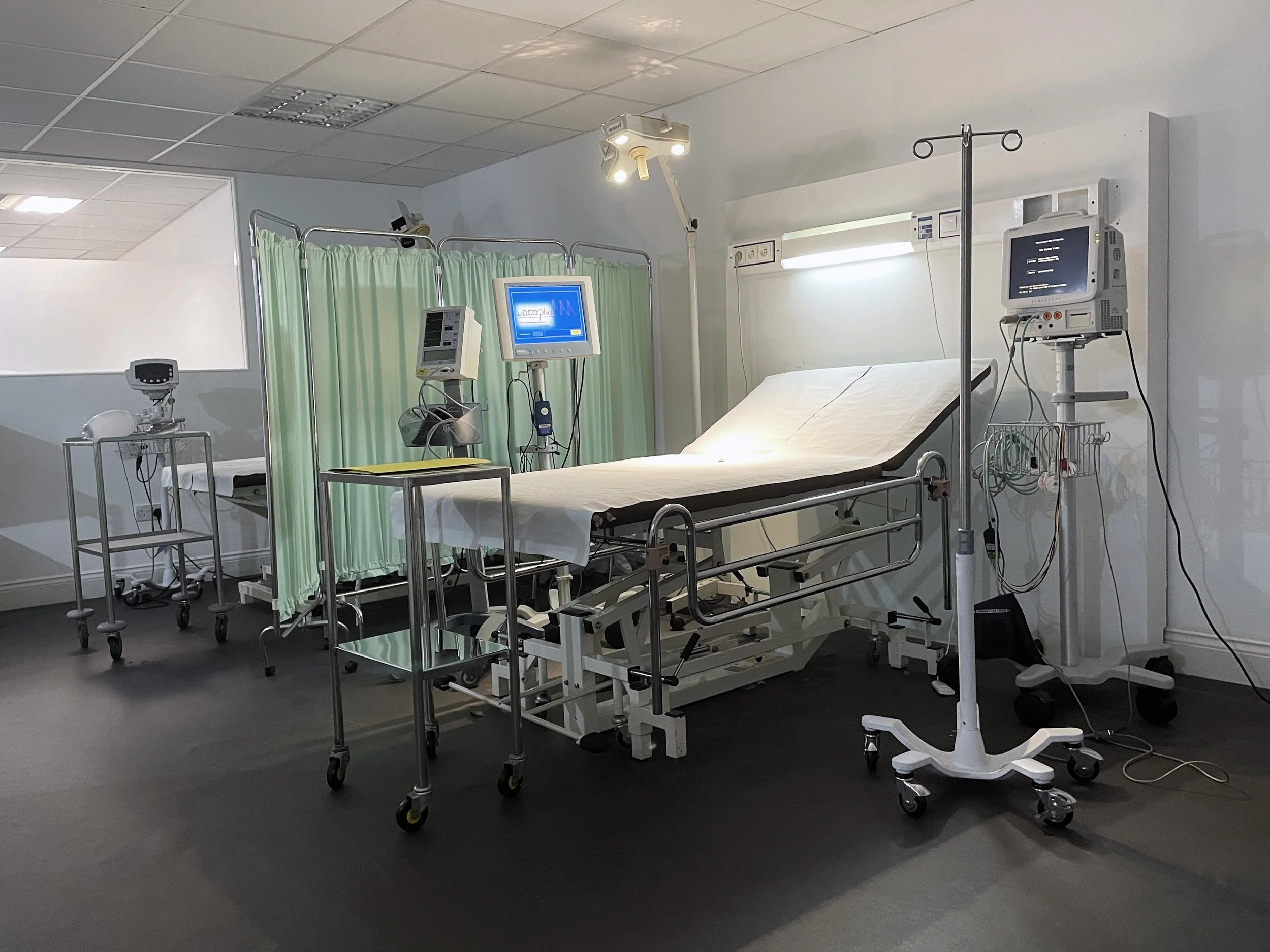 A hospital emergency room with a hospital bed, medical monitors, IV stand, and privacy curtain.