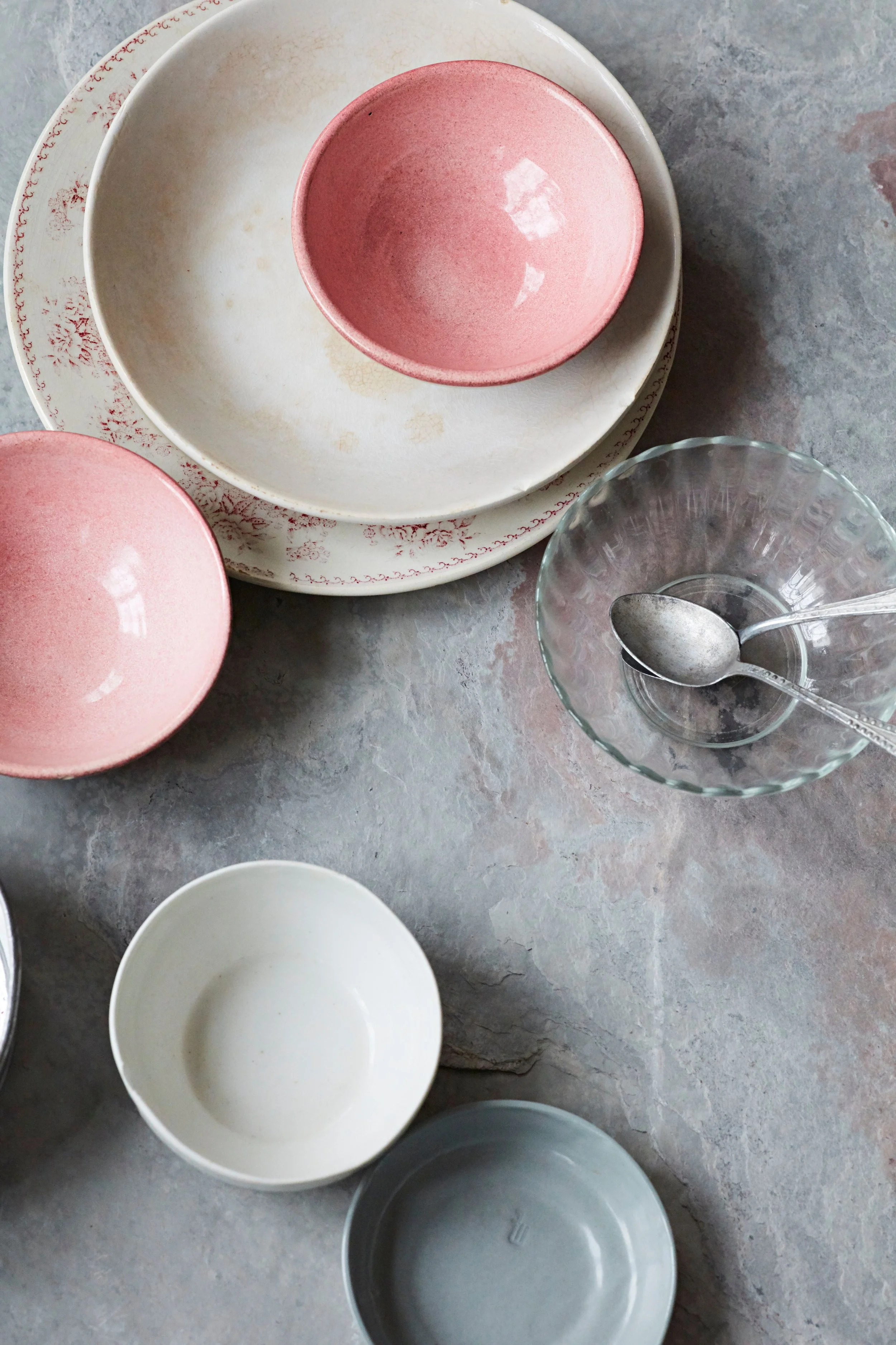 Various empty bowls and a glass dish with a spoon on a stone surface.