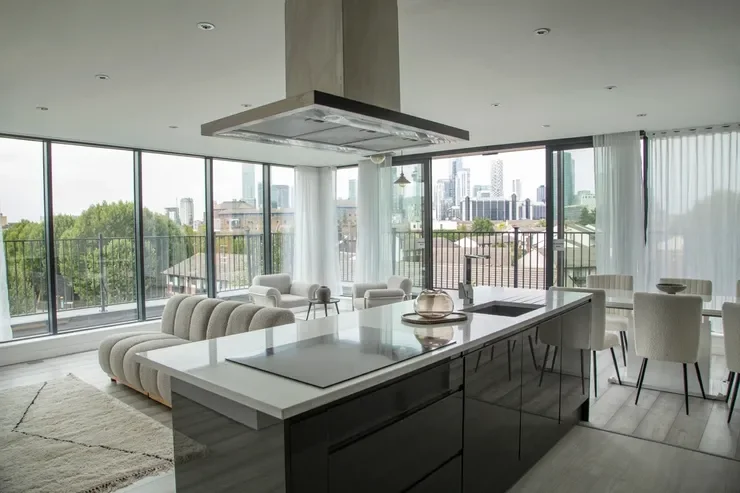 Modern open-concept apartment with a kitchen island, dining area, and living space, large windows with city and greenery views.