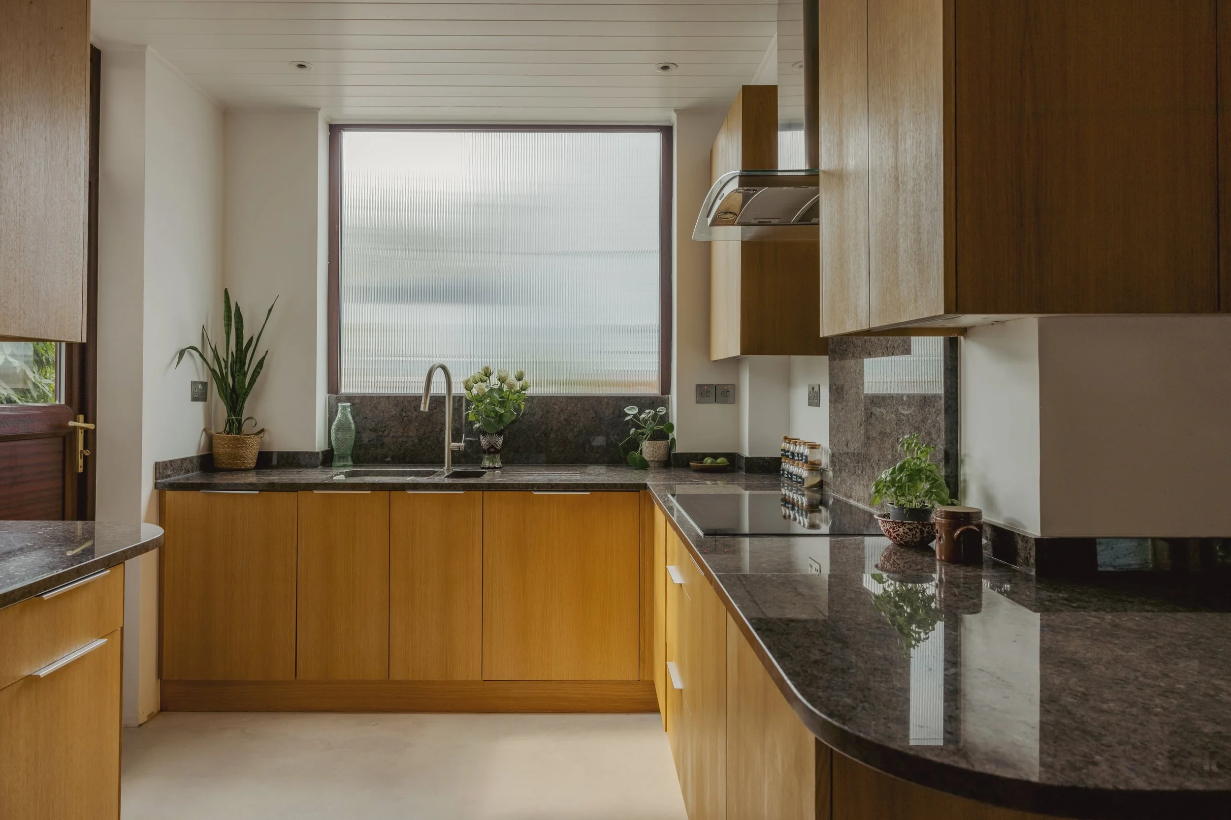 Kitchen with wooden cabinets, black granite countertops, a window above the sink, and decorative plants.